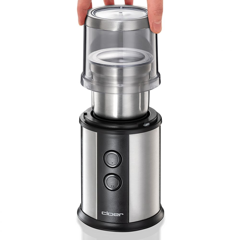 Ręka podnosi pokrywę młynka do kawy, odsłaniając wnętrze młynka.