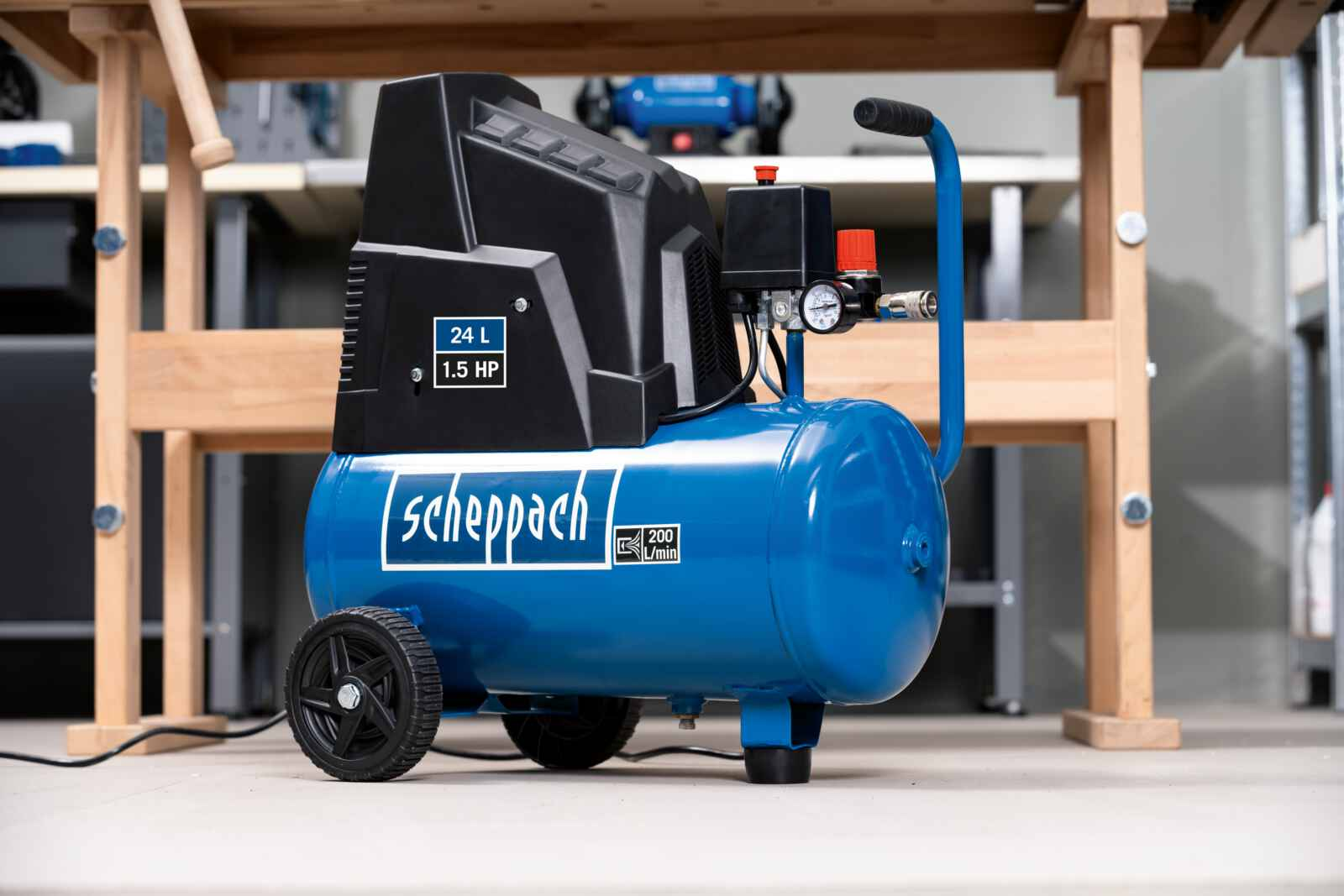 Compressore d'aria blu e nero con ruote. È su un pavimento di cemento davanti a una mensola di legno.