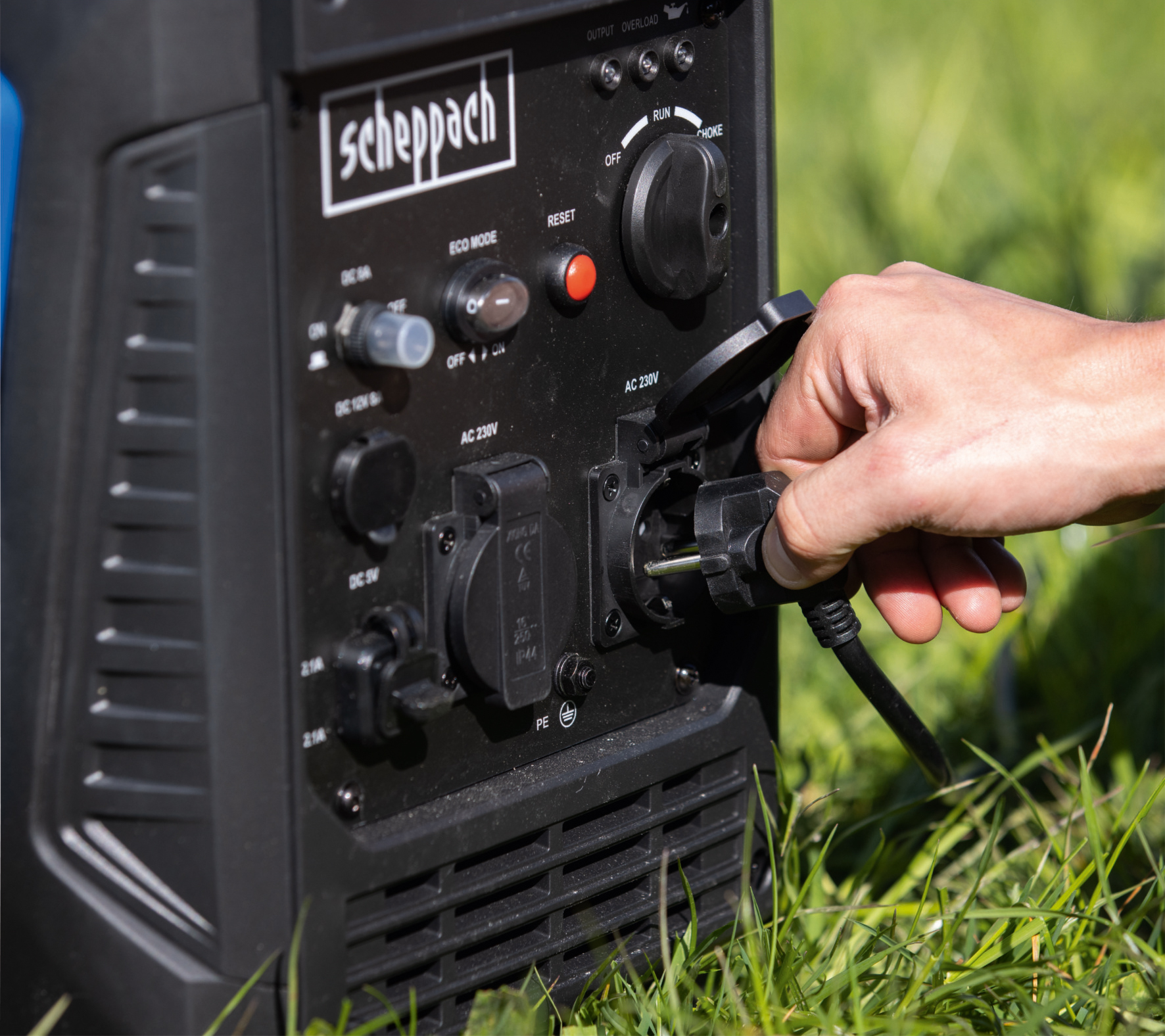Een hand steekt een zwarte kabel in een zwarte generatorpoort op gras.
