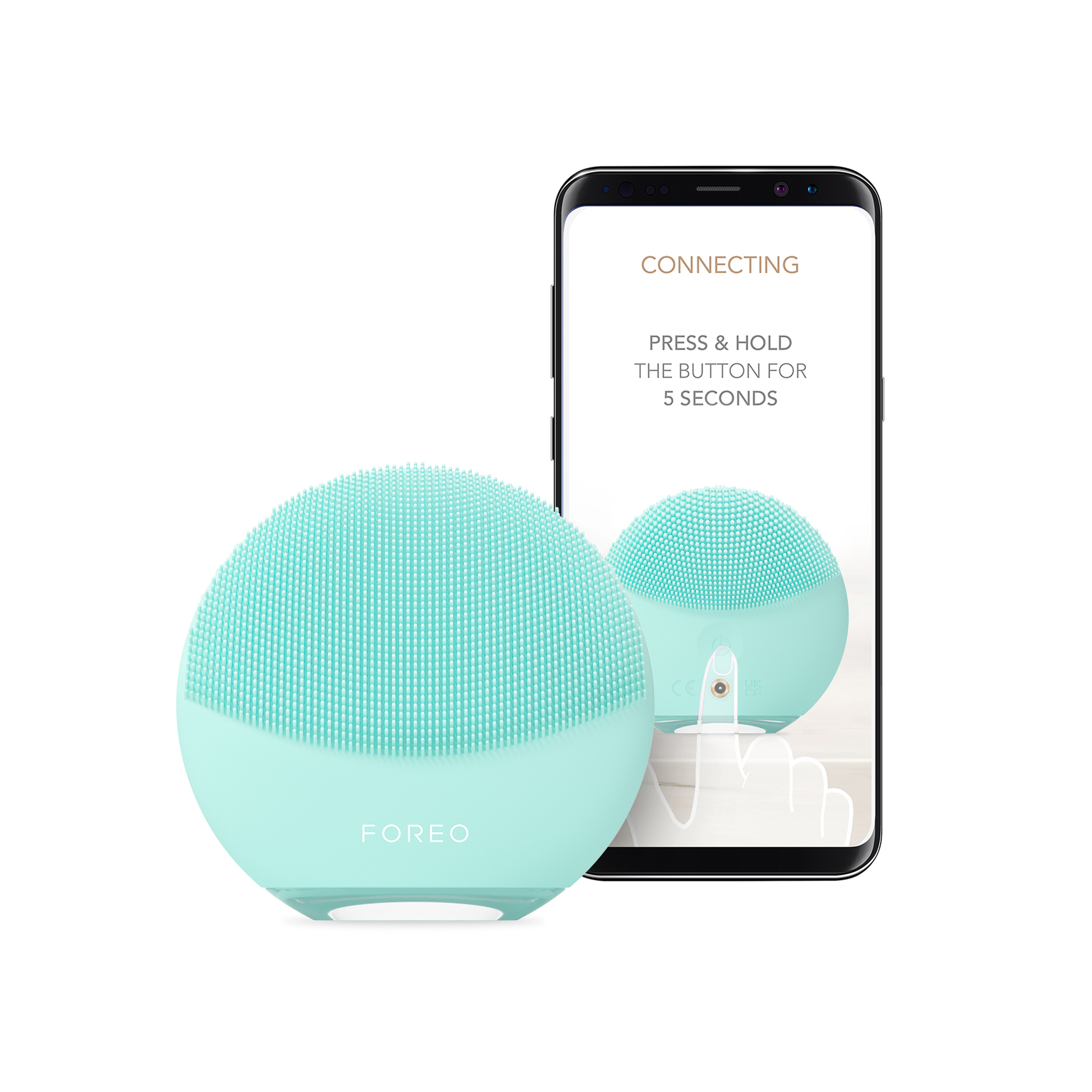 A mint green face cleanser device beside a phone displaying instructions, on a white surface.