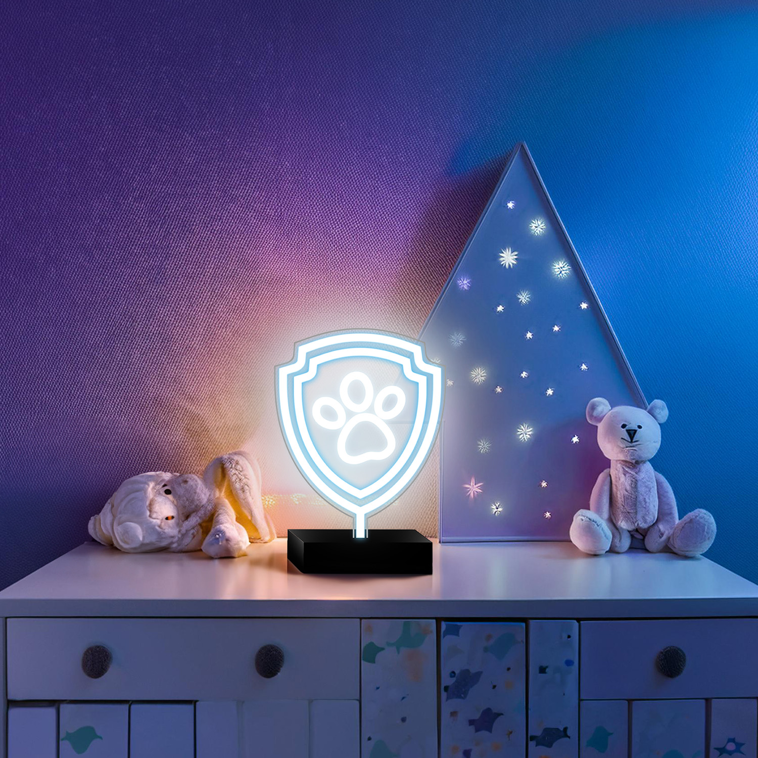 Neonowy znak Paw Patrol na stoliku nocnym z zabawkami, łóżkiem i dekoracją w kształcie choinki.