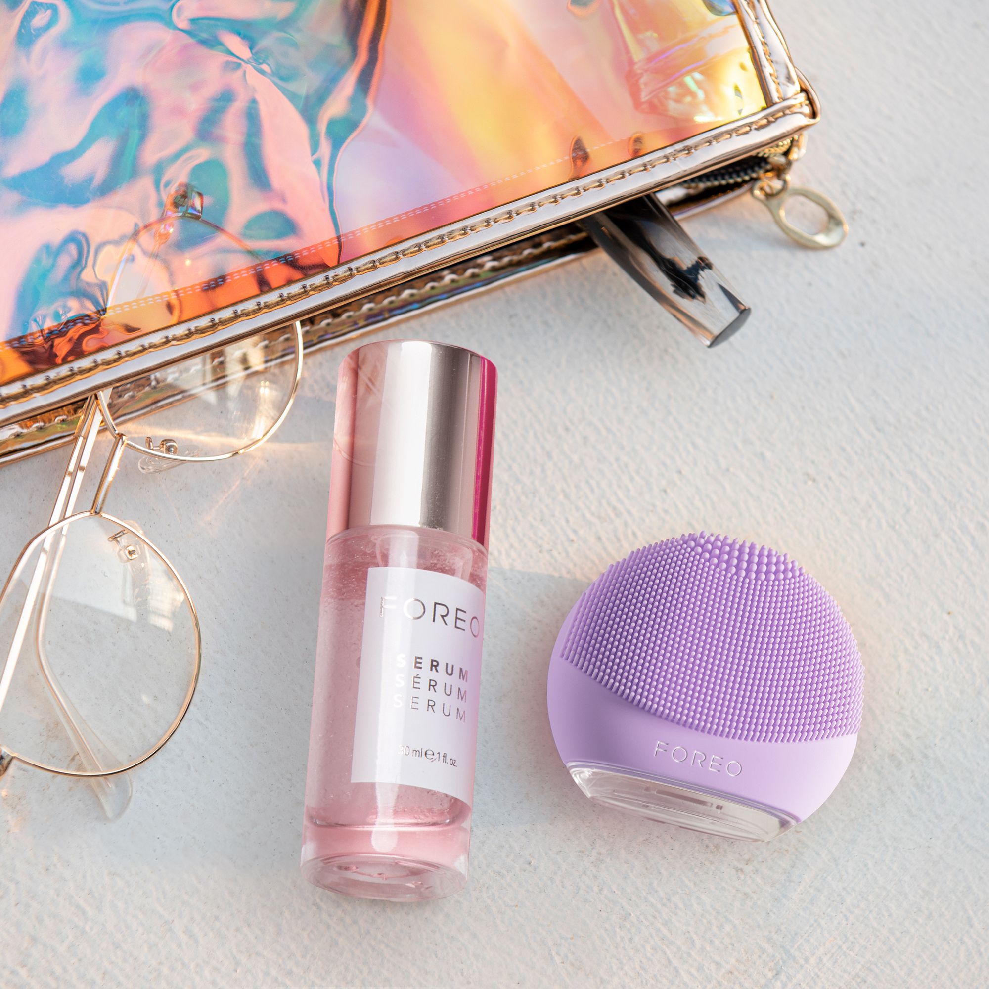 Cosmetic products, glasses, and a cosmetic bag on a white surface. The background is blurred.