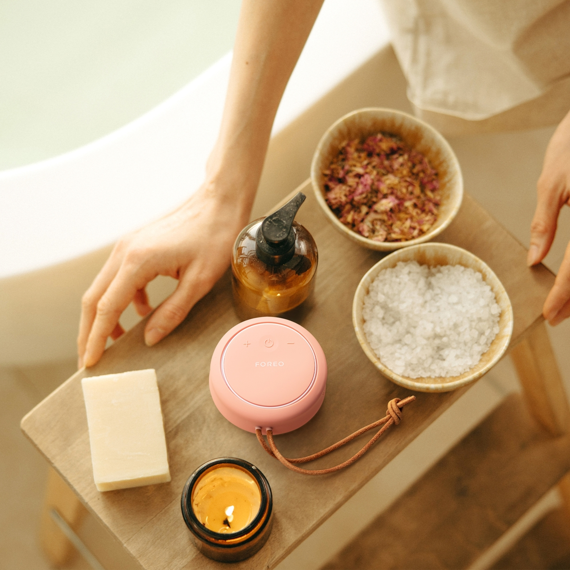 Pembe güzellik cihazı ve diğer spa ürünleri ahşap bir tepside. Beyaz banyo zemini.