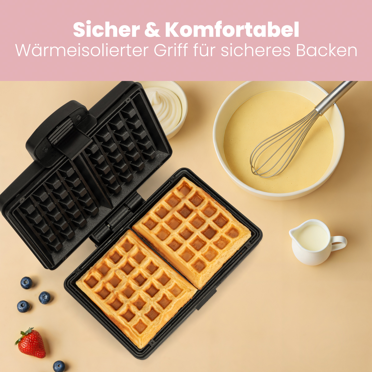 Otwarta gofrownica z goframi, ciastem, śmietaną i borówkami na beżowym tle.