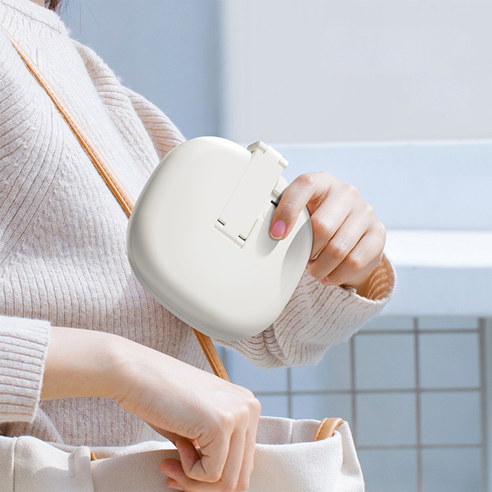 Eine Person, die einen weißen tragbaren Ventilator mit Riemen hält, neben einer Handtasche.