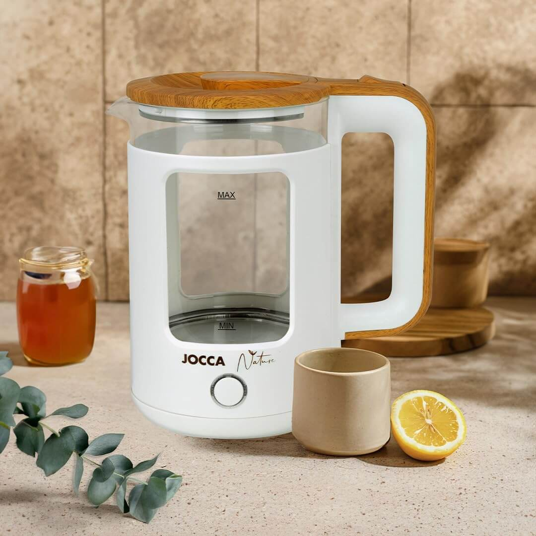 Weißer Wasserkocher mit Holzakzenten. Eine Teetasse, ein Honigglas und eine Zitrone stehen auf der Theke.