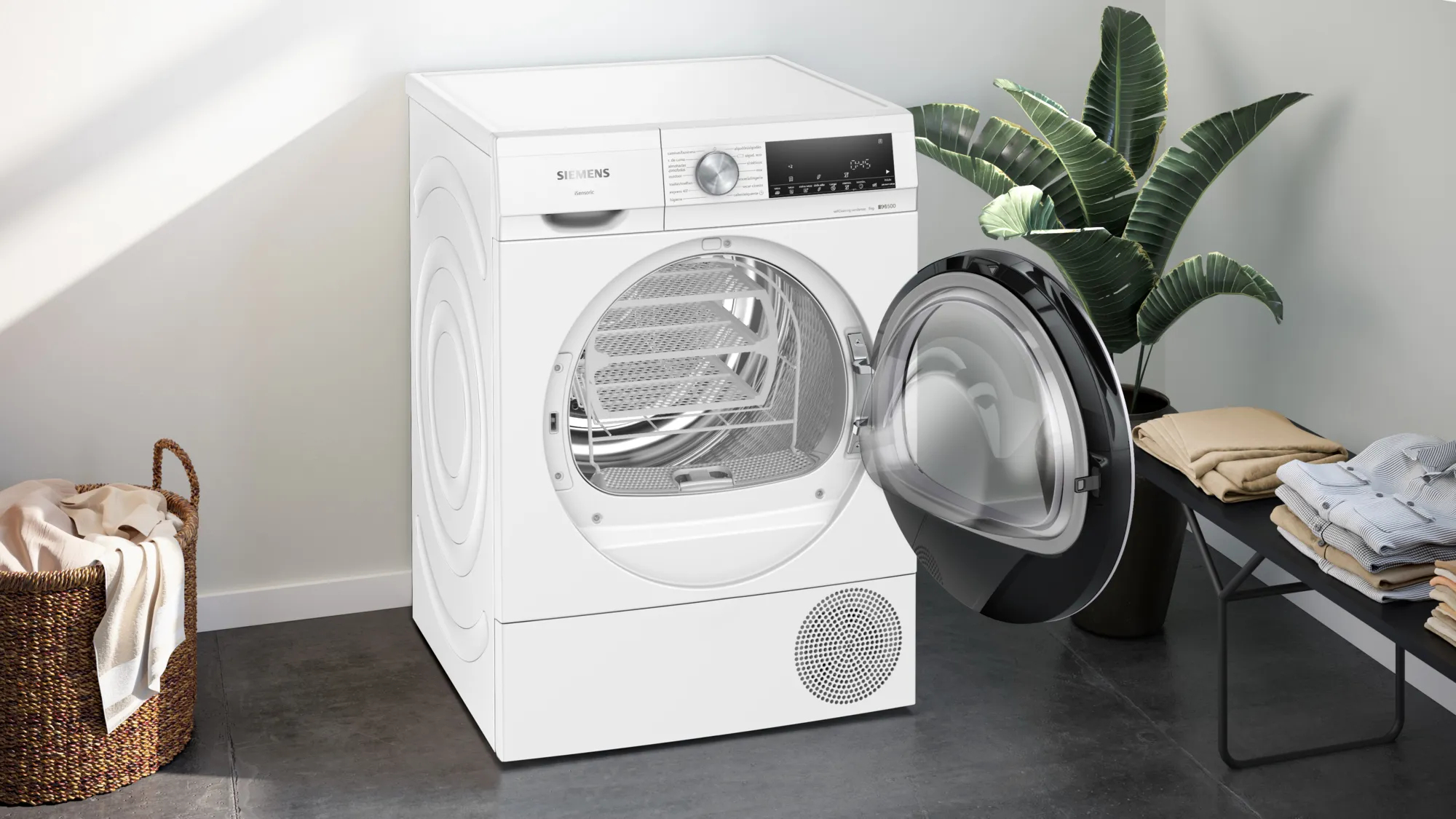 Een witte droger met open deur naast een mand en plant.