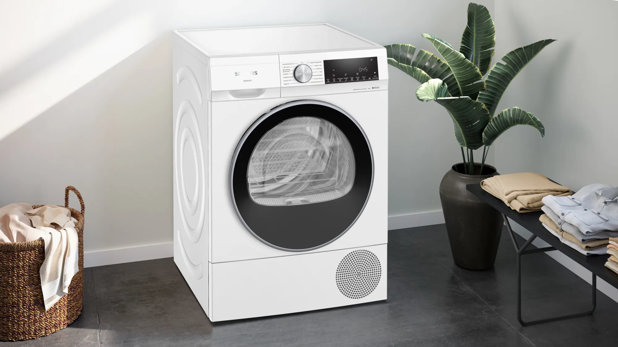 Witte Siemens droger in een kamer met een plant en mand. De droger heeft een zwarte deur.
