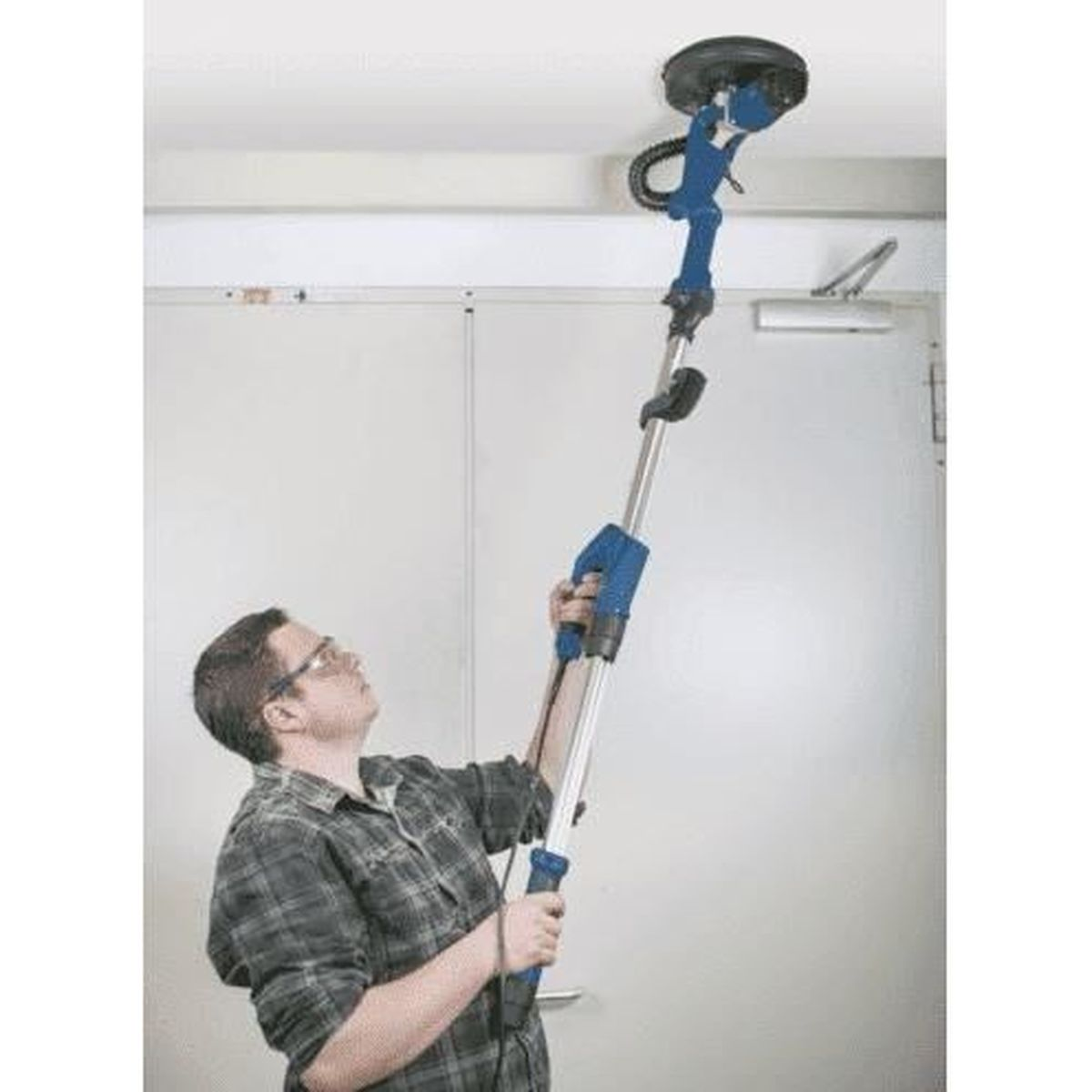 Uomo usa levigatrice blu e argento su soffitto bianco. Indossa occhiali.