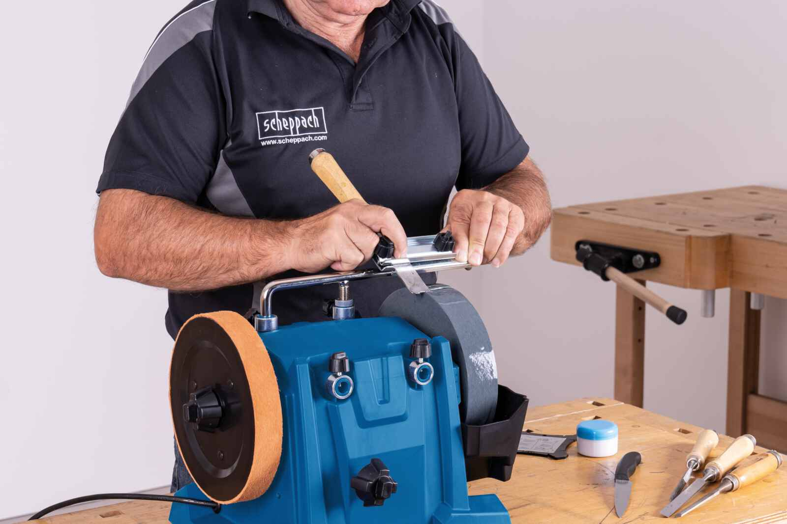 Una persona sta affilando uno strumento su una smerigliatrice blu su una superficie di legno.