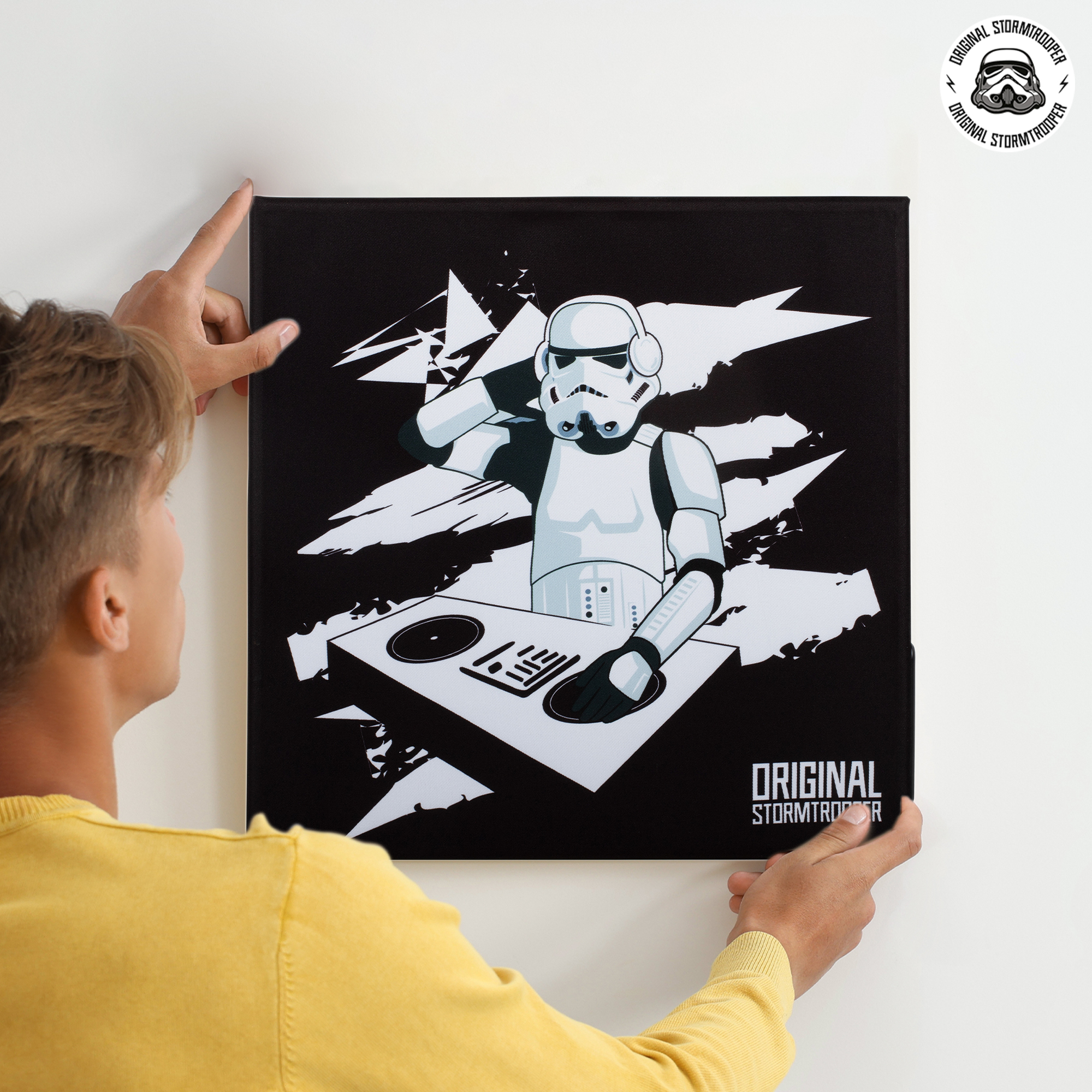 Een persoon hangt een Stormtrooper DJ-canvas op een witte muur. Het logo staat rechtsboven.