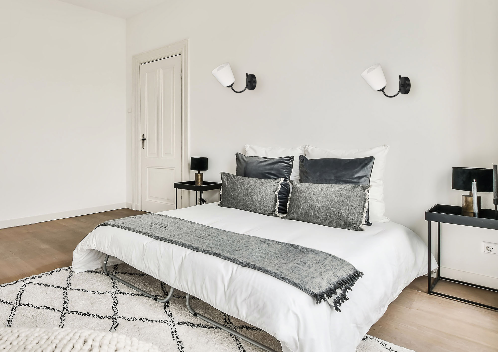 Una camera da letto con letto, due comodini, due lampade da parete e pareti bianche.