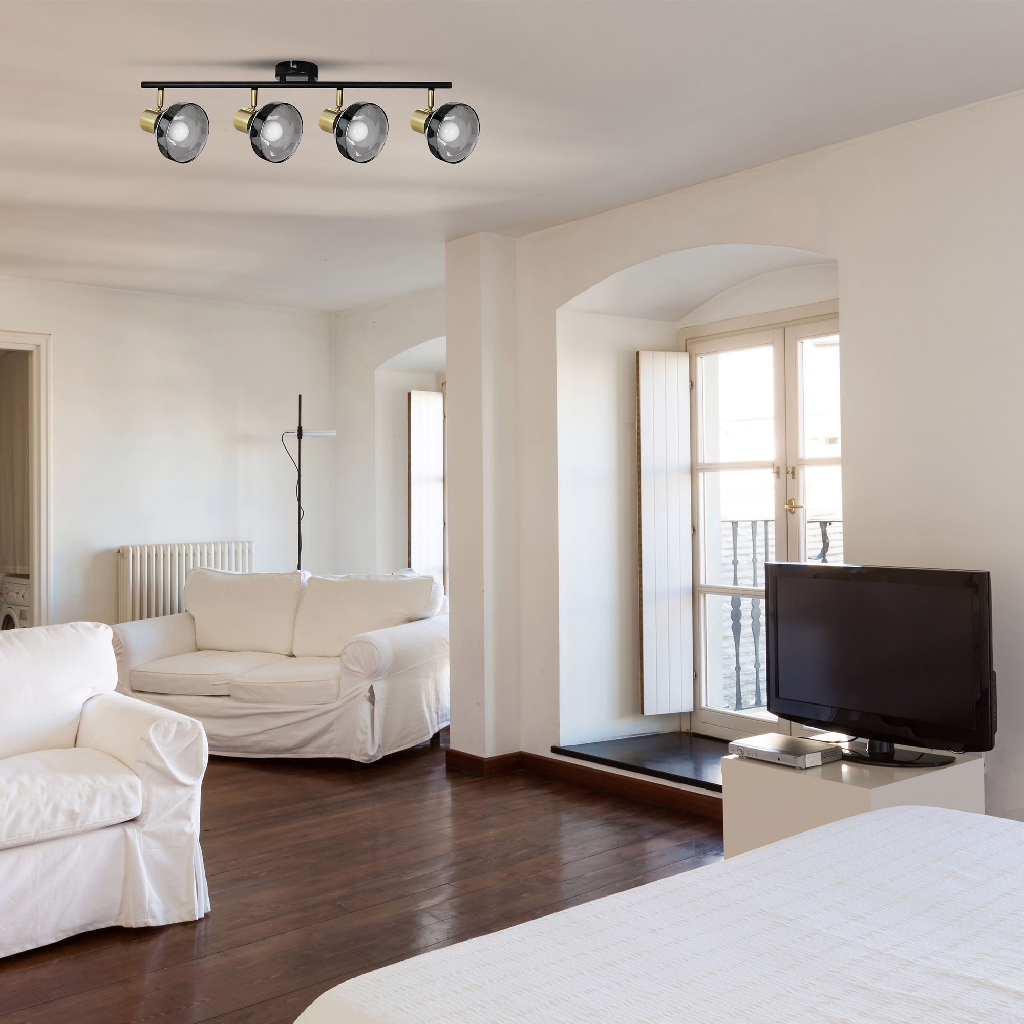 Salón moderno con sofá, TV y focos de techo. Suelo de madera oscura, paredes blancas.