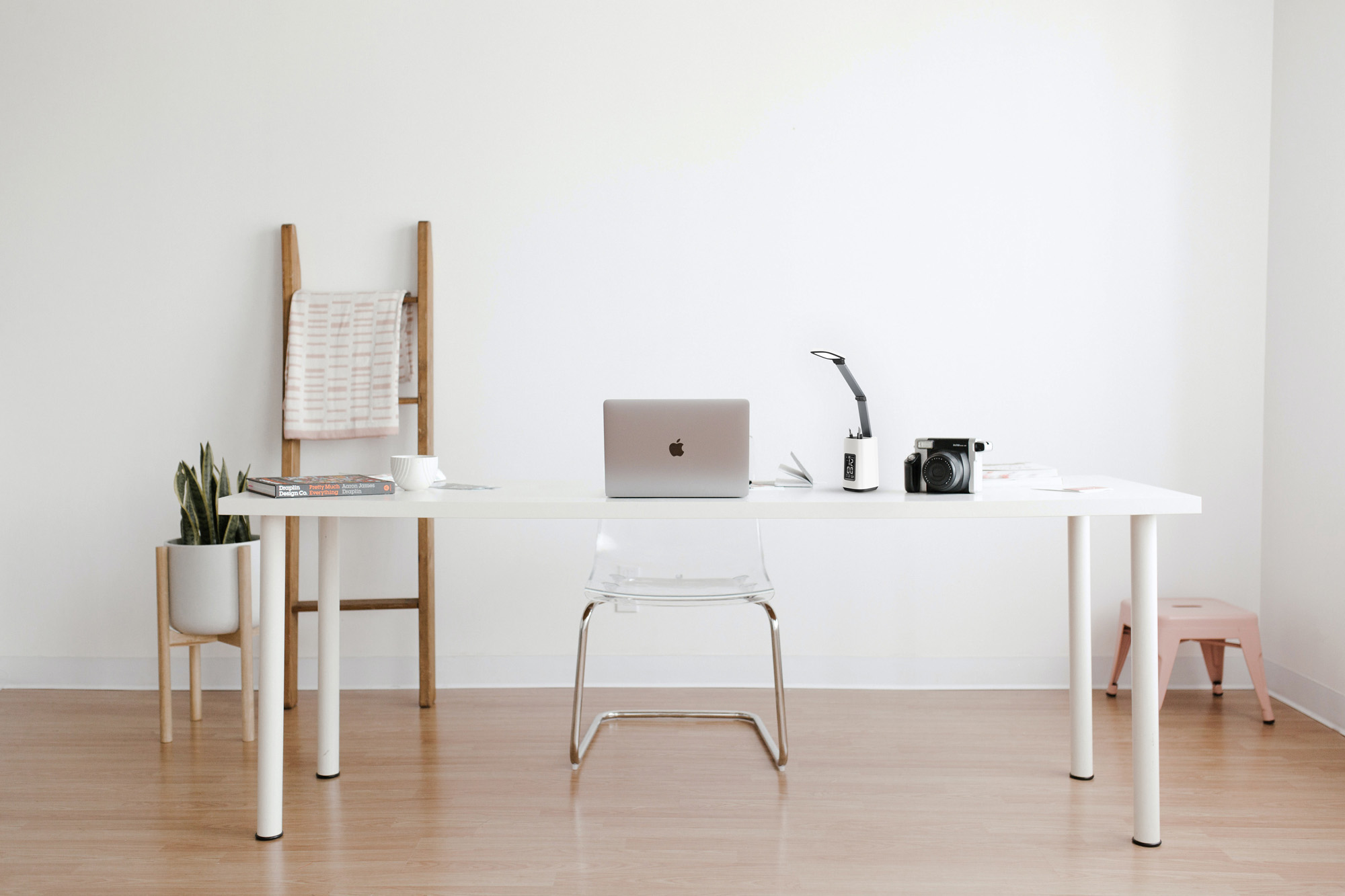 Białe biurko z laptopem, krzesłem i przedmiotami. Drabina z ręcznikiem opiera się o ścianę.