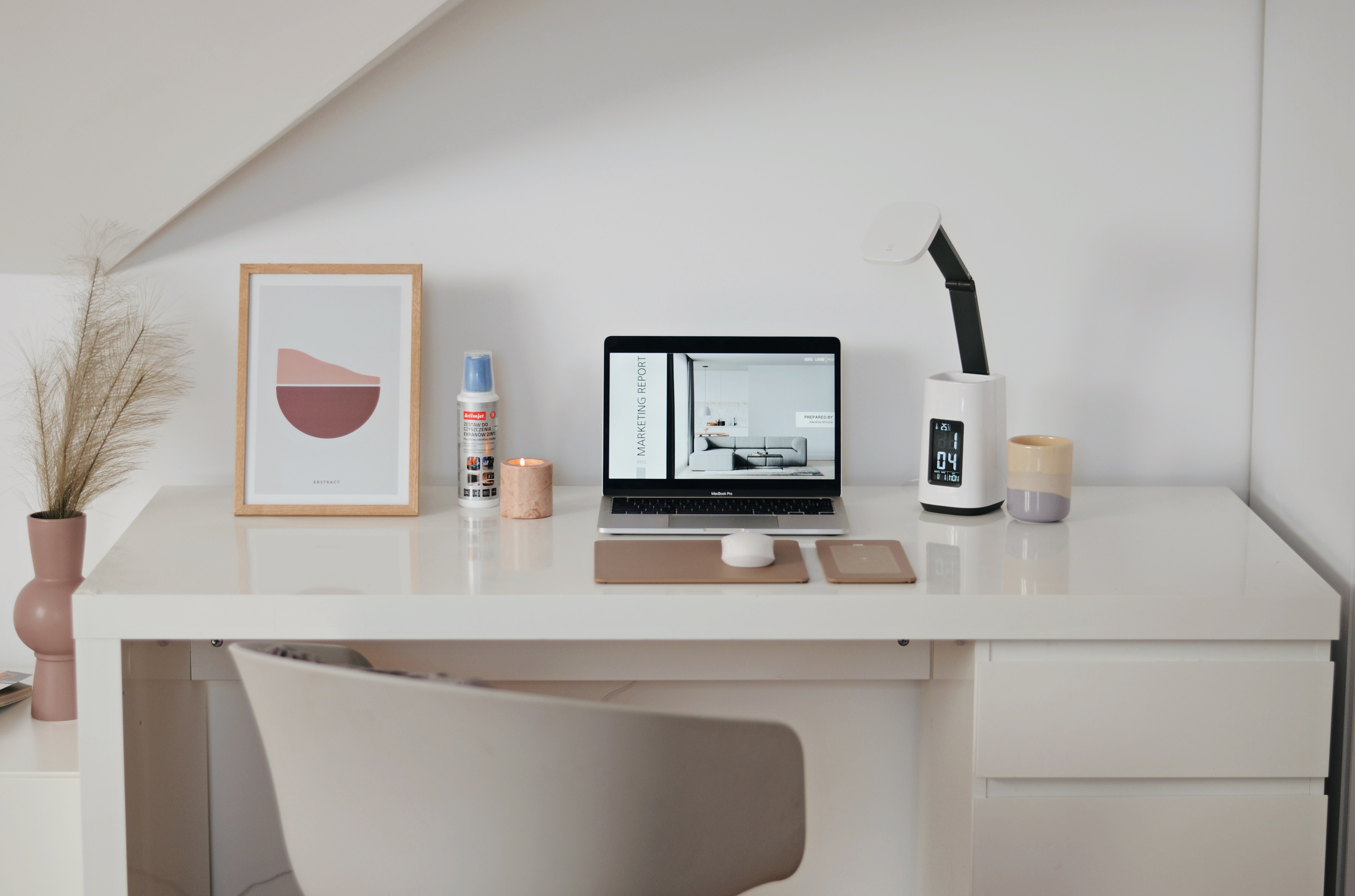 Białe biurko z laptopem wyświetlającym raport marketingowy, lampą i dekoracjami.