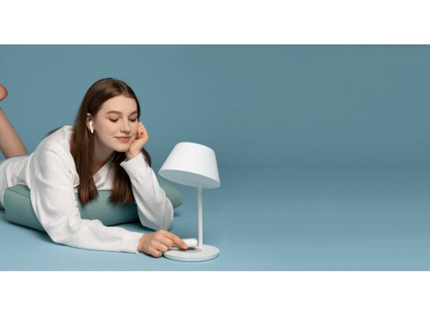 Kobieta leży na poduszce z białymi słuchawkami w uszach. Lampa jest po prawej stronie.