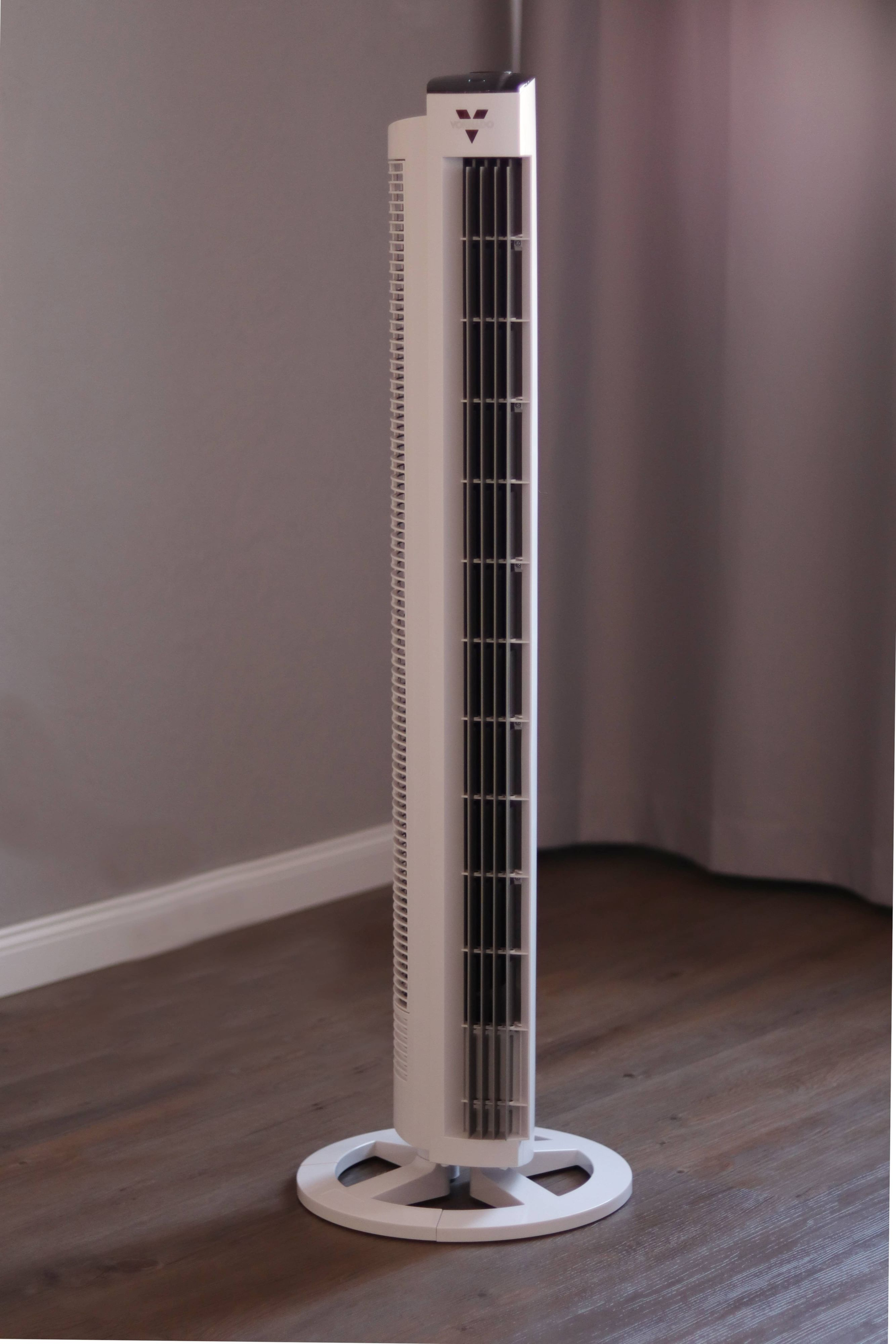 Hoher weißer Vornado-Ventilator in einer Ecke. Der Hintergrund ist eine graue Wand und ein Vorhang.