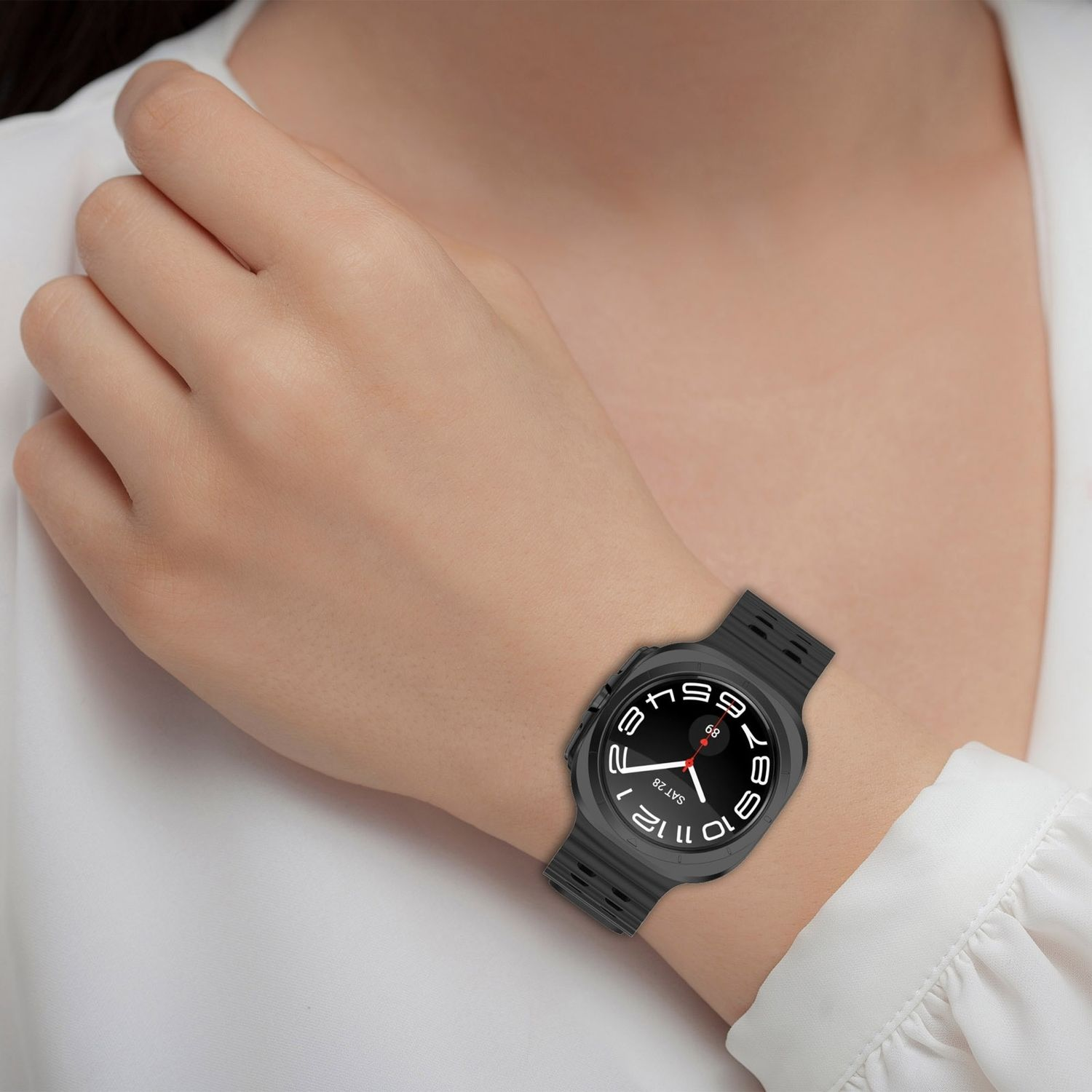 Das Handgelenk einer Frau mit einer schwarzen Smartwatch, vor weißem Hemdhintergrund.