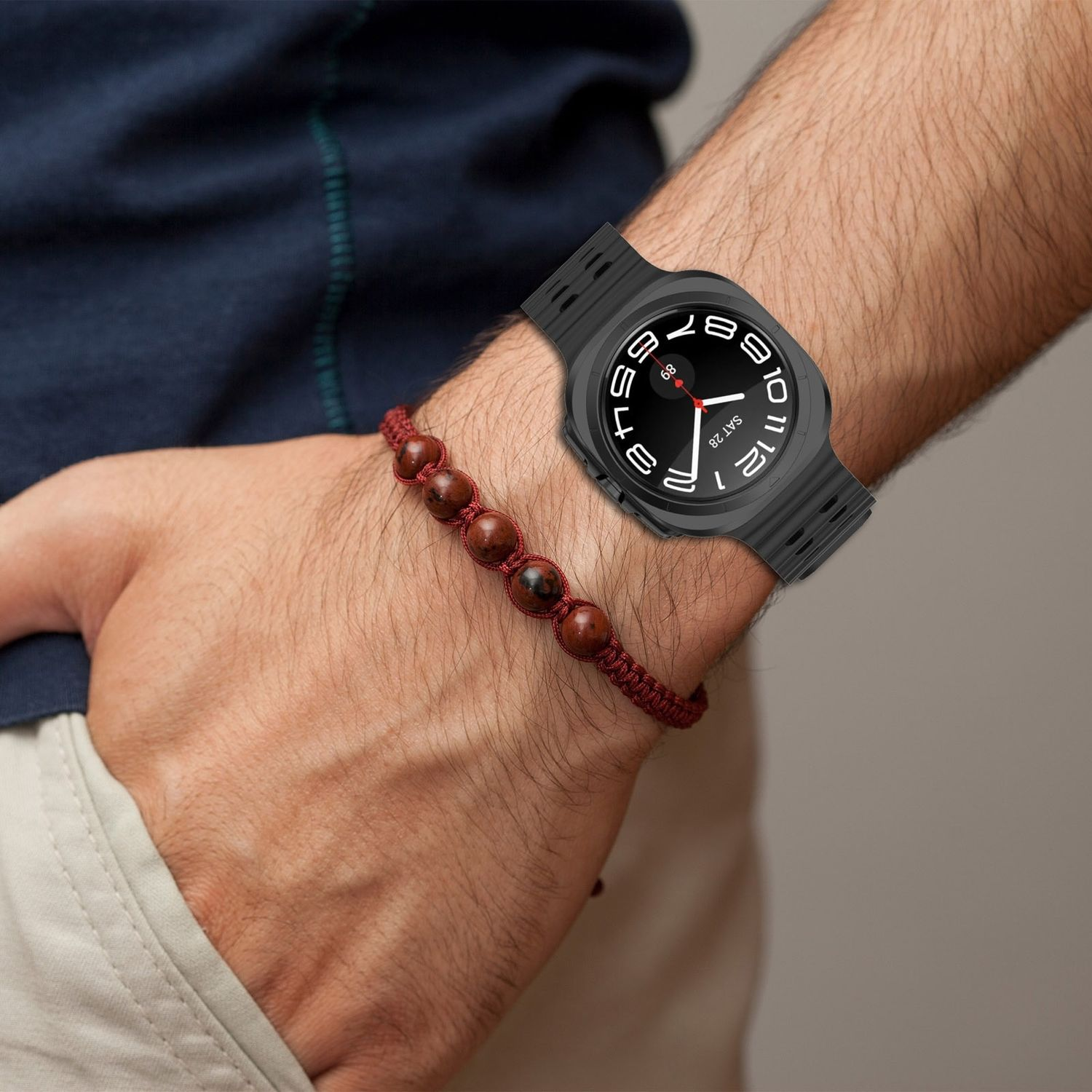 Eine Person trägt eine schwarze Smartwatch mit einem roten Perlenarmband am Handgelenk.