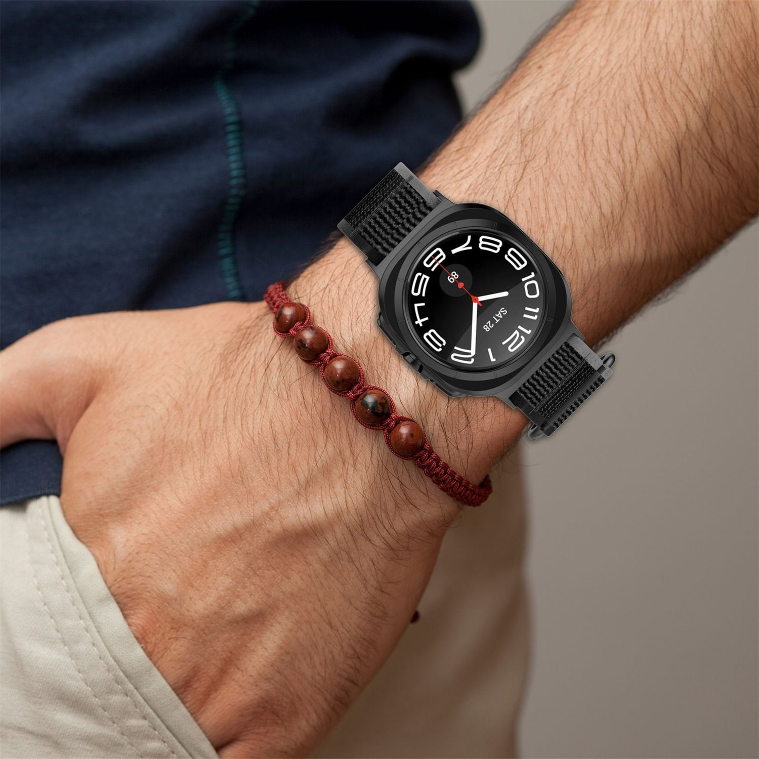Person trägt eine schwarze Smartwatch und ein braunes Perlenarmband am Handgelenk.