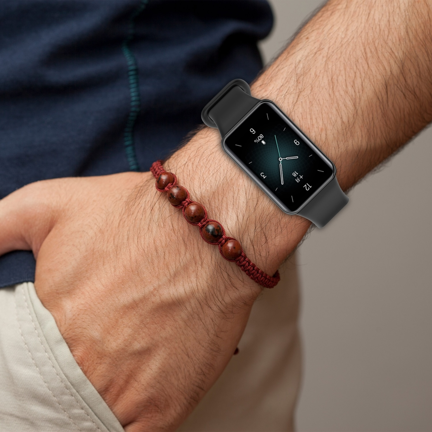 Das Handgelenk einer Person mit einer Smartwatch und einem roten Perlenarmband.