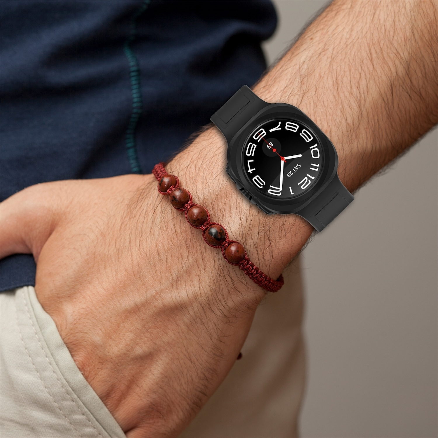 Il polso di una persona con uno smartwatch nero e un braccialetto di perline rosse.