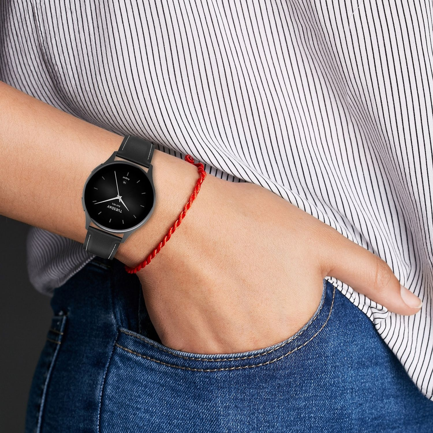 Das Handgelenk einer Person mit einer Uhr und einem roten Armband, mit gestreiftem Hemd und Jeans.