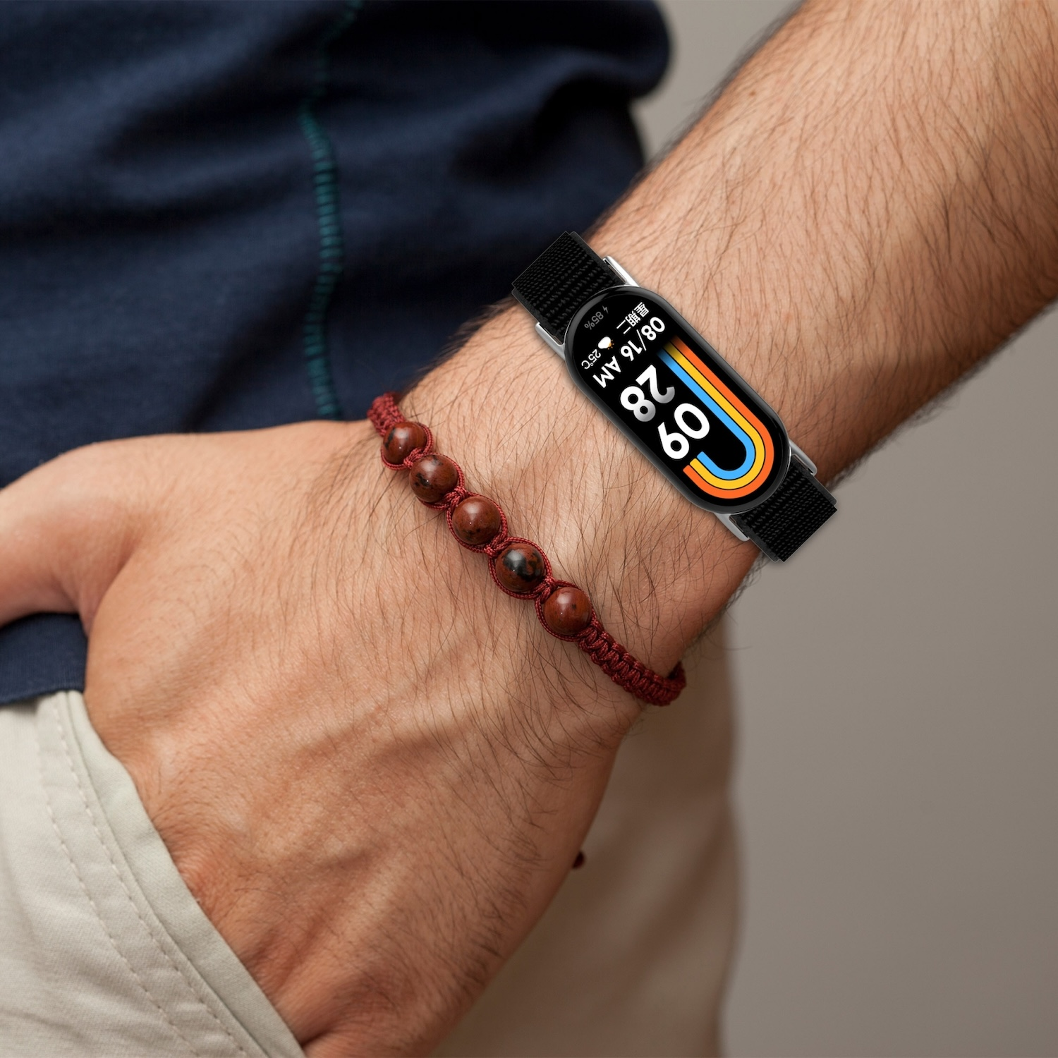 Person trägt Fitness-Tracker am Handgelenk und rotes Perlenarmband am Arm.