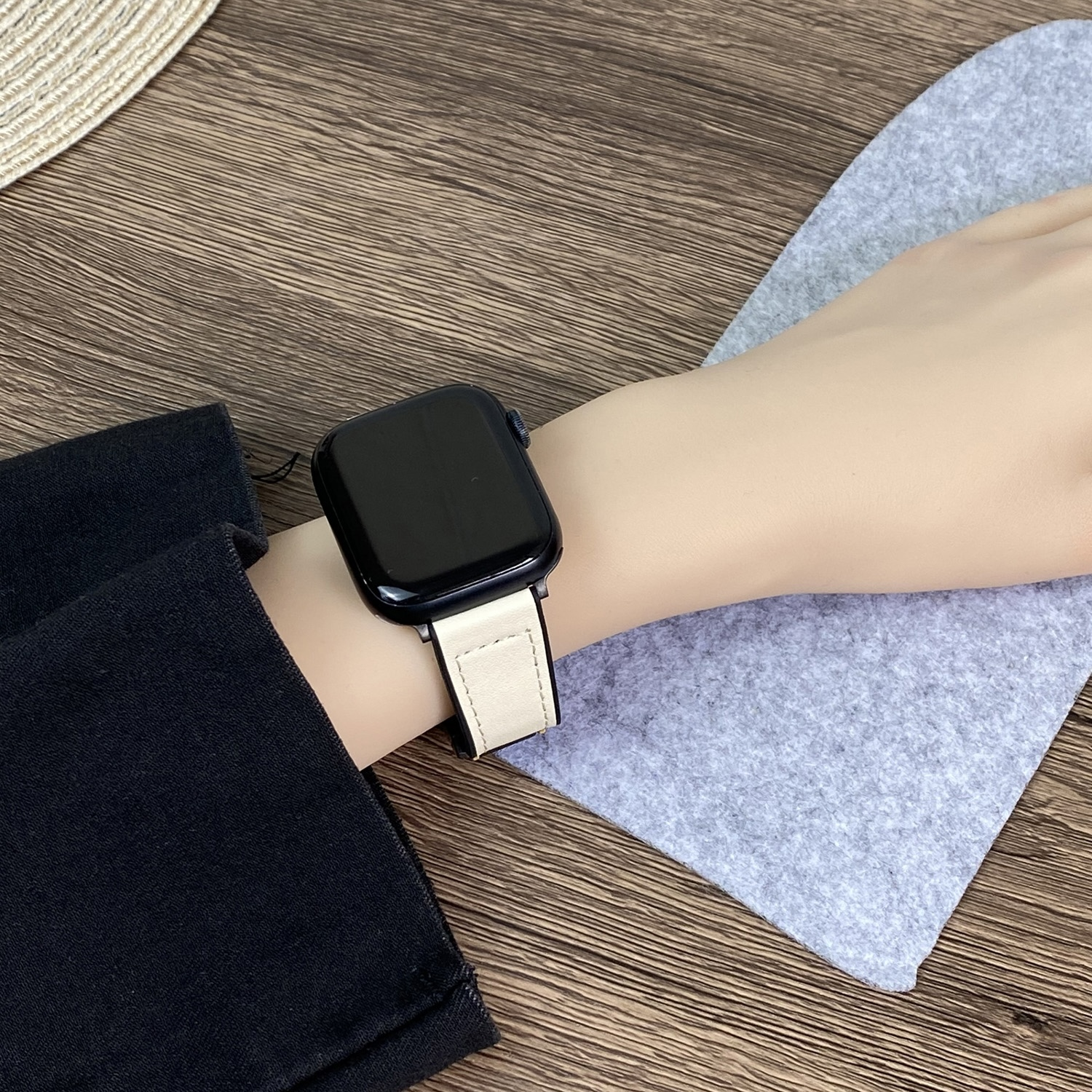 Handgelenk einer Frau mit einer schwarzen Smartwatch und einem cremefarbenen Armband. Holzgrund.