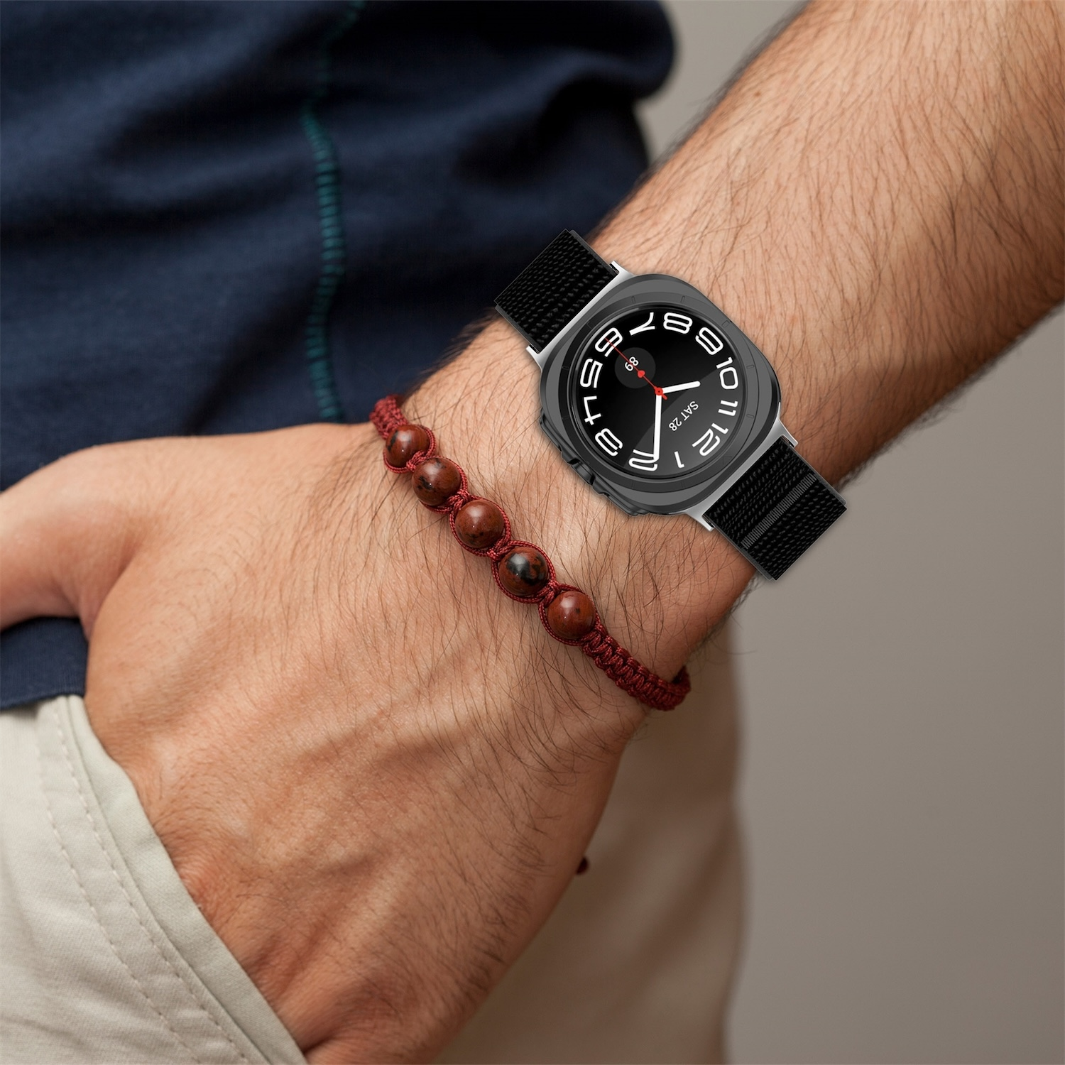 Mann trägt eine Uhr mit schwarzem Band und ein rotes Perlenarmband. Der Mann trägt ein blaues Hemd.