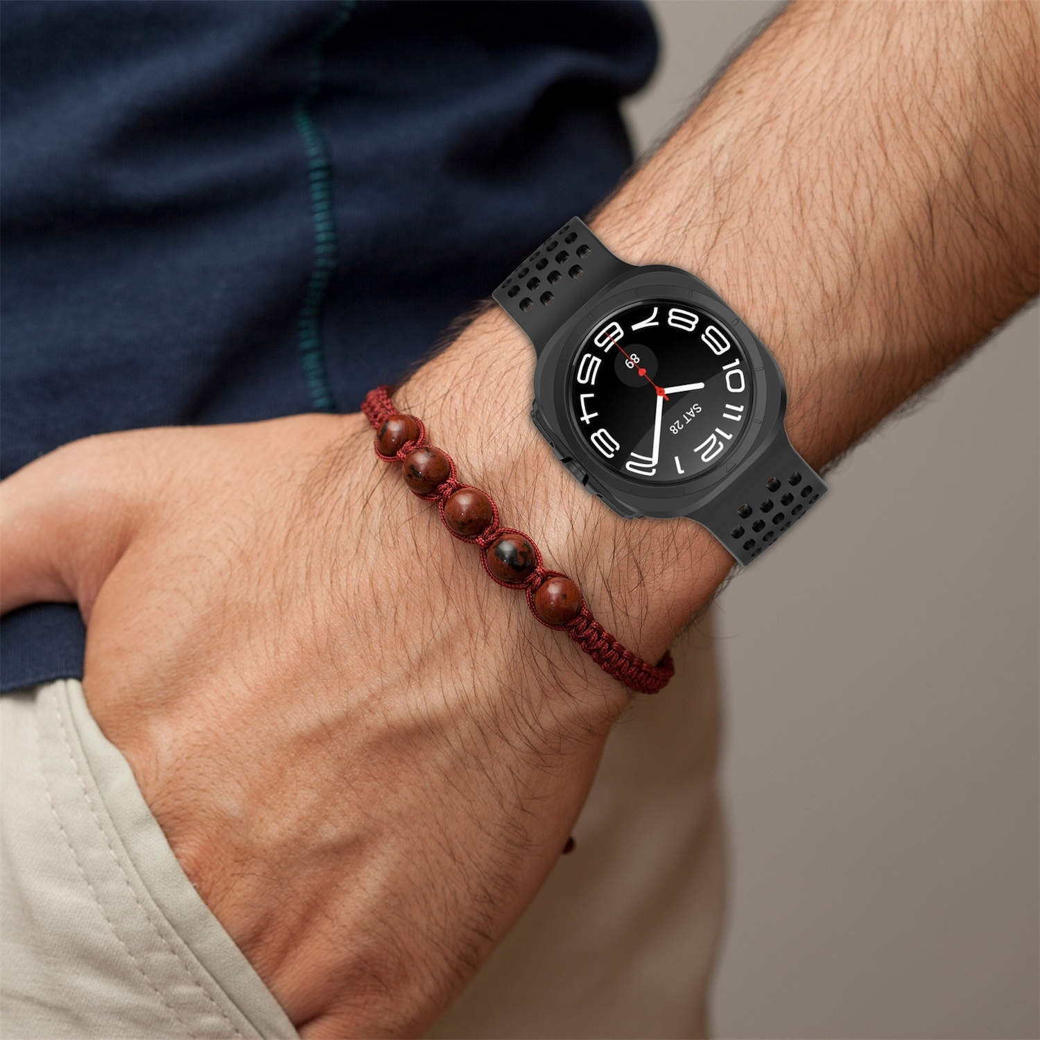 Person trägt Smartwatch mit schwarzem Gehäuse und rotem Band, sowie Armband. Nahaufnahme.