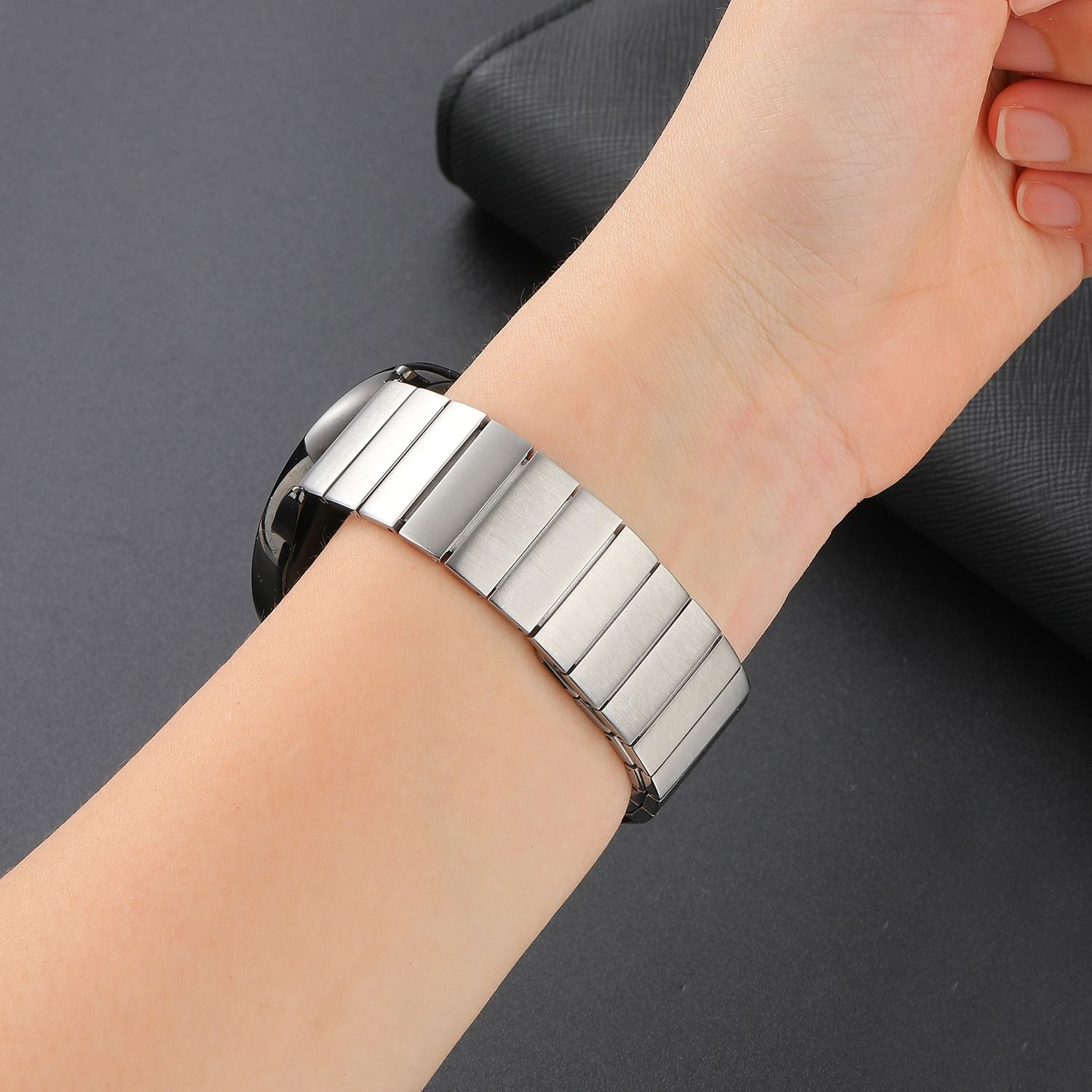 Das Handgelenk einer Person mit einem silbernen Metalluhrenarmband. Das Band ist rechteckig.