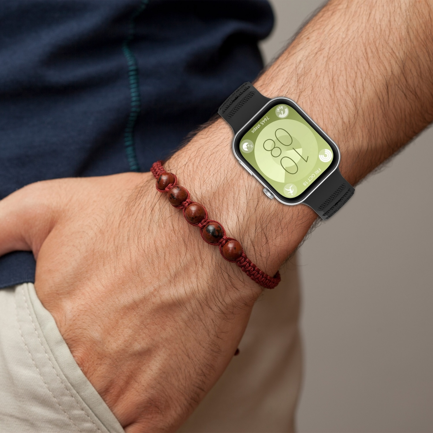Das Handgelenk einer Person mit einer Smartwatch und einem roten Perlenarmband. Die Uhr zeigt die Zeit.