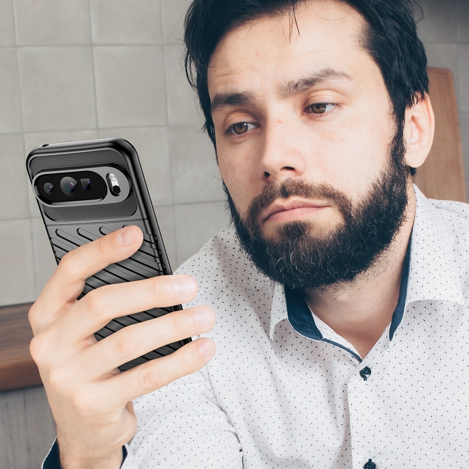 Mann mit Bart, der auf ein Telefon in einer schwarzen, robusten Hülle blickt.