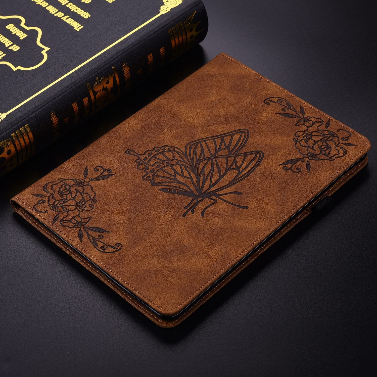 Funda marrón para tableta con diseño de mariposa y flores. Libro visible en el fondo.