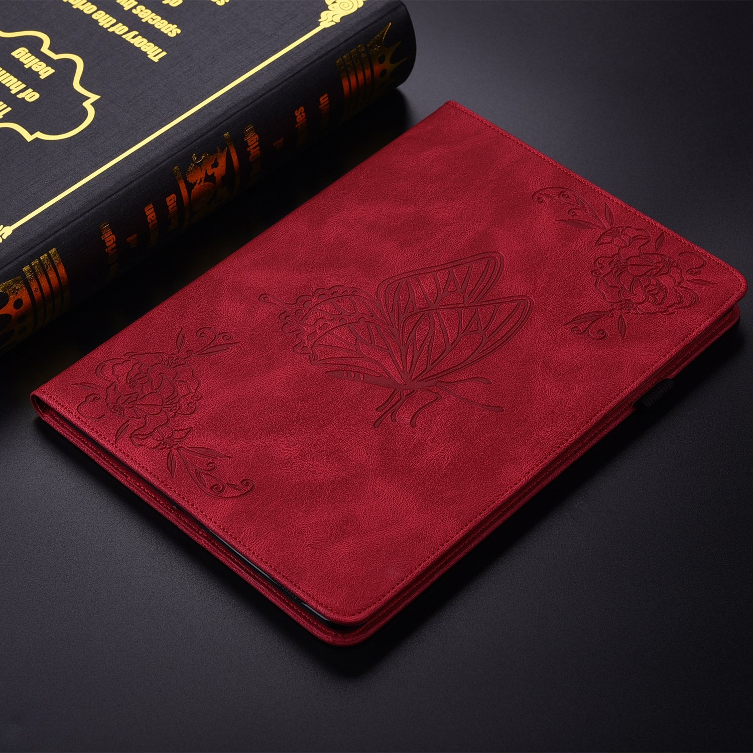 Funda de tableta roja con diseño de mariposa. Un libro también está en la escena.