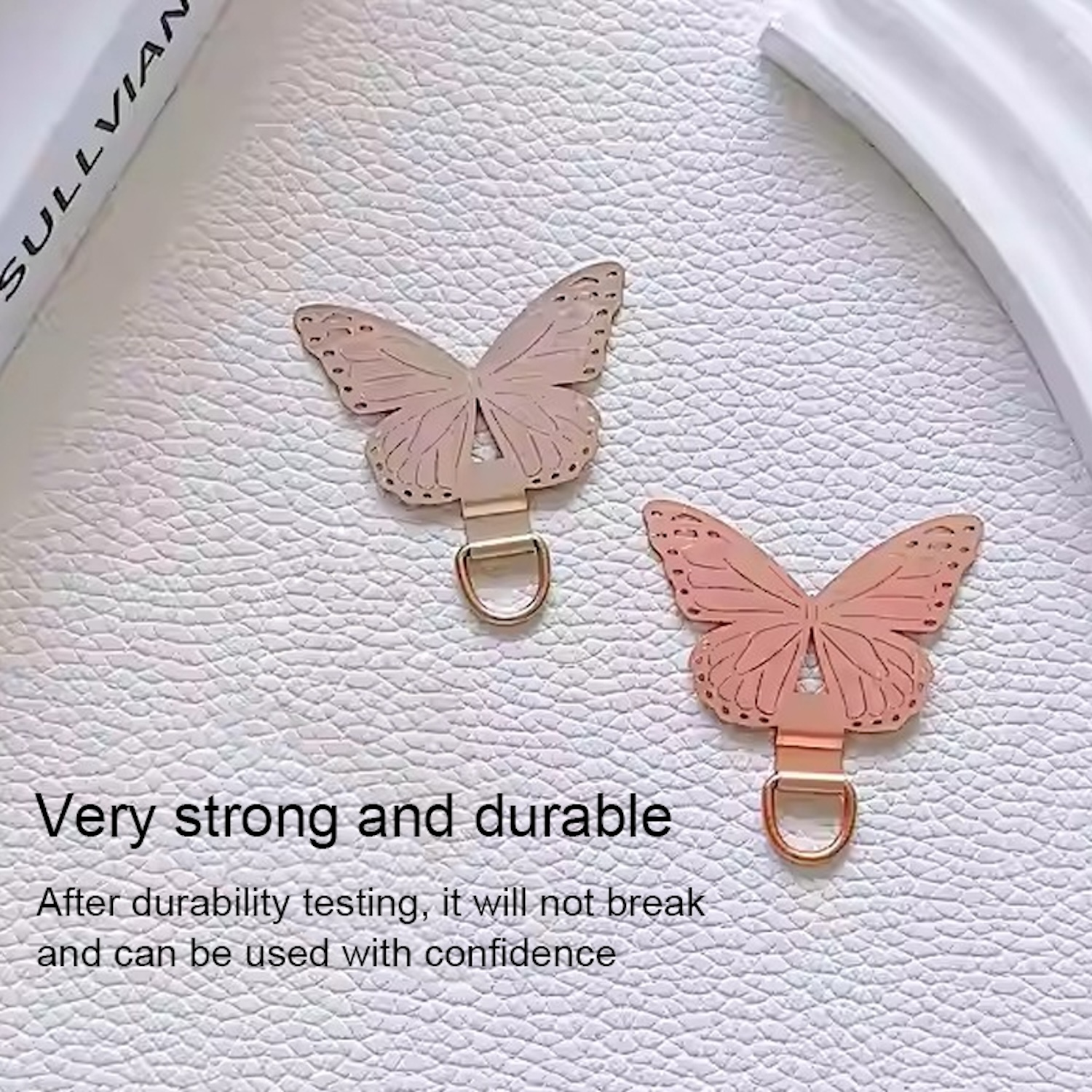 Zwei roségoldene Schmetterlingsanhänger mit Ringverschluss auf cremefarbener Oberfläche.