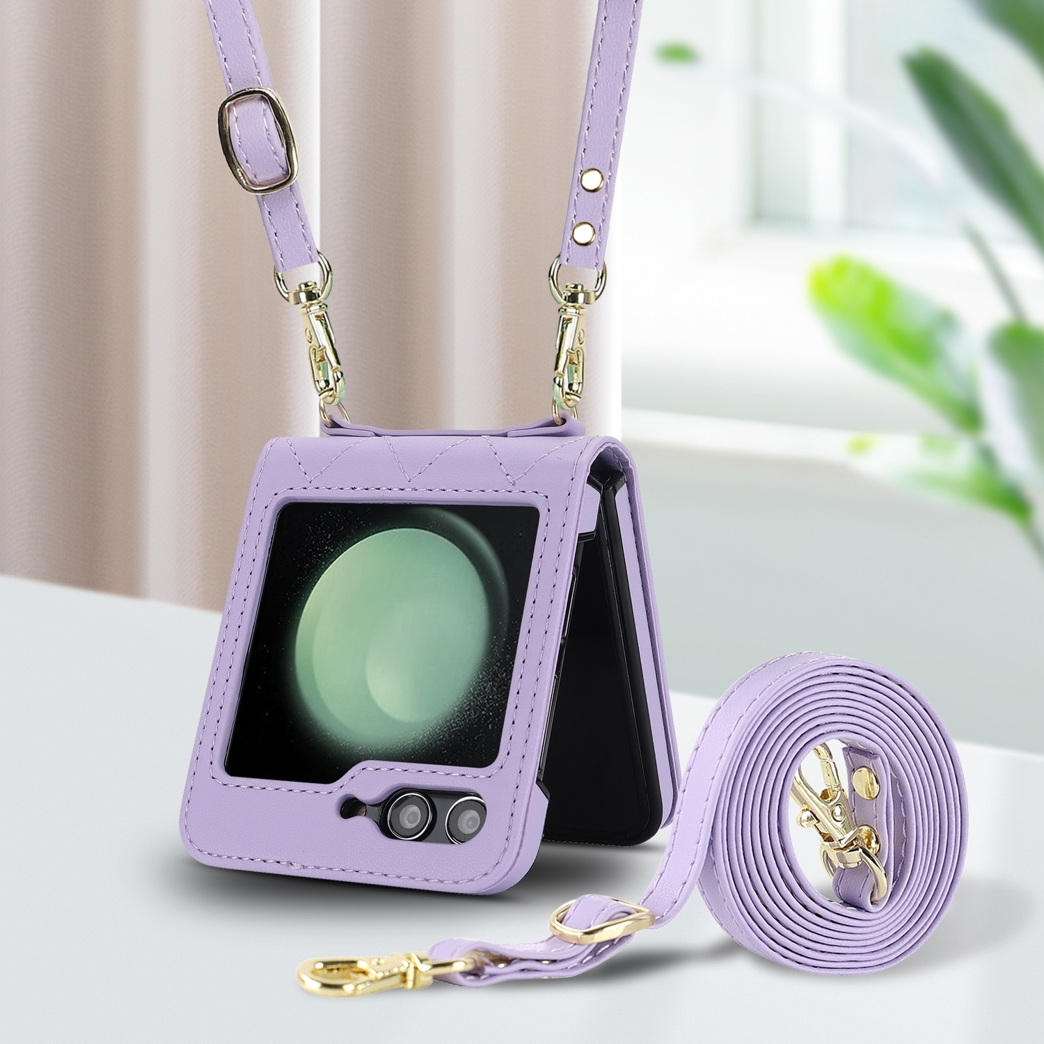 Funda de teléfono morada con correa, sosteniendo un teléfono. Herrajes dorados. Fondo borroso.