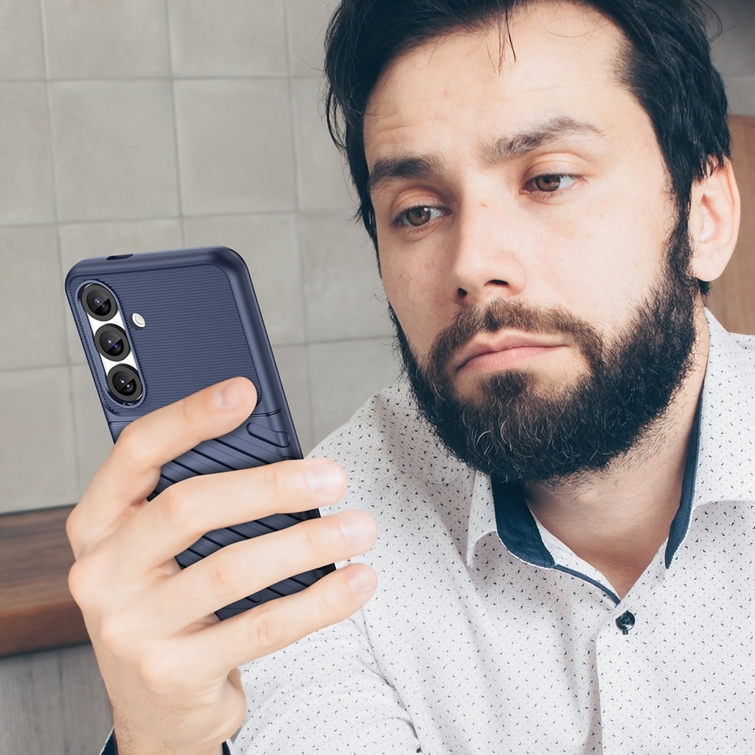Ein Mann, der auf sein Telefon schaut, welches sich in einer dunkelblauen Hülle befindet.