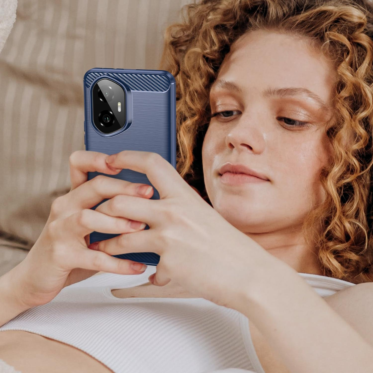 Frau hält blaues Telefon mit Hülle, liegt im Bett. Lockiges Haar und weißes Oberteil sichtbar.