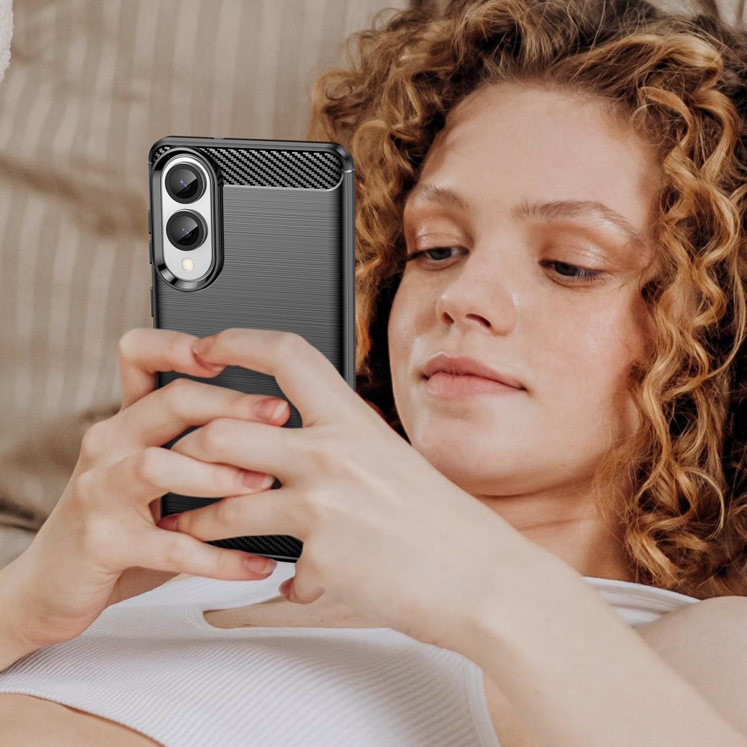 Una mujer sostiene un teléfono en sus manos, mirando la pantalla. El teléfono tiene una funda negra y texturizada.