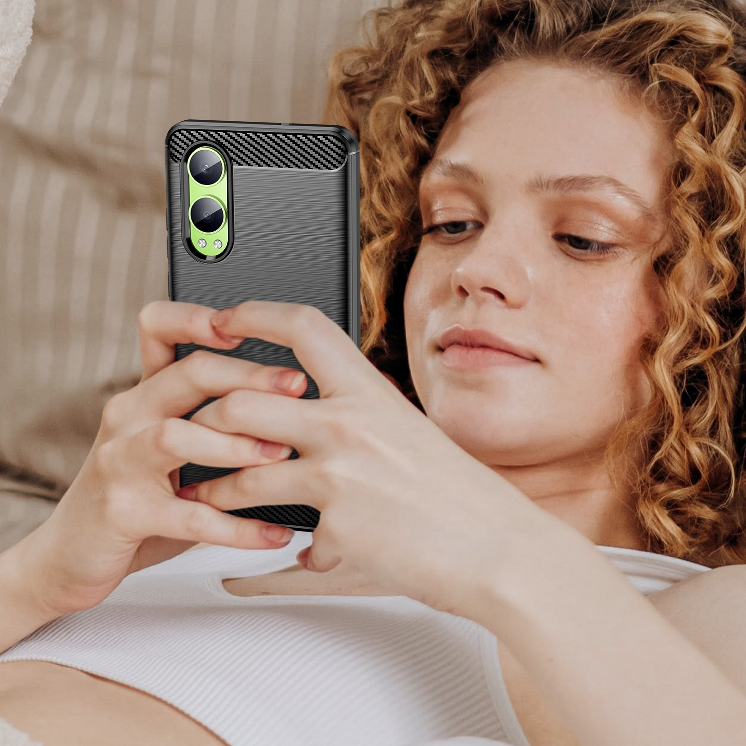 Una mujer con cabello rizado sostiene un teléfono con una funda negra, que tiene una parte trasera texturizada.