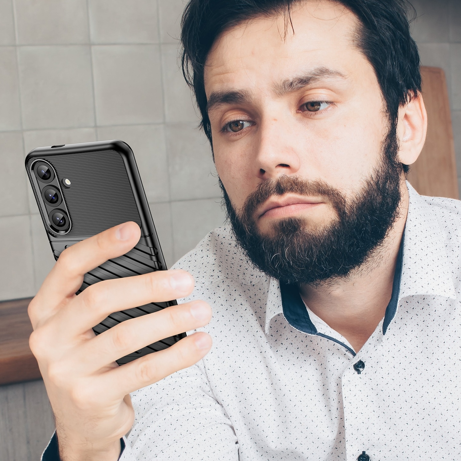 Ein Mann, der auf sein Telefon schaut, das eine schwarze Hülle hat. Die Hülle hat ein strukturiertes Design.