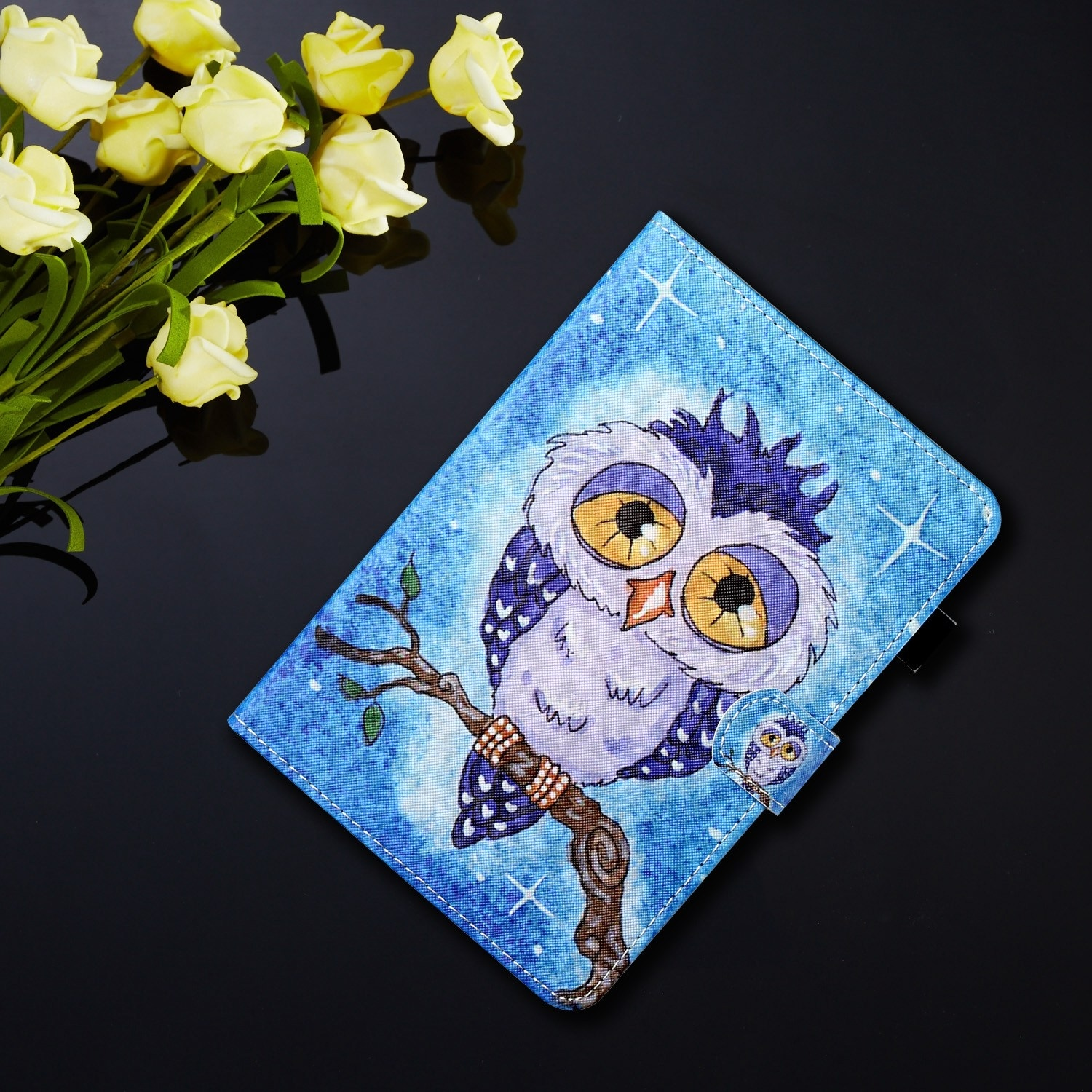 Ilustración de búho en una funda azul. Sobre una superficie negra con flores amarillas.