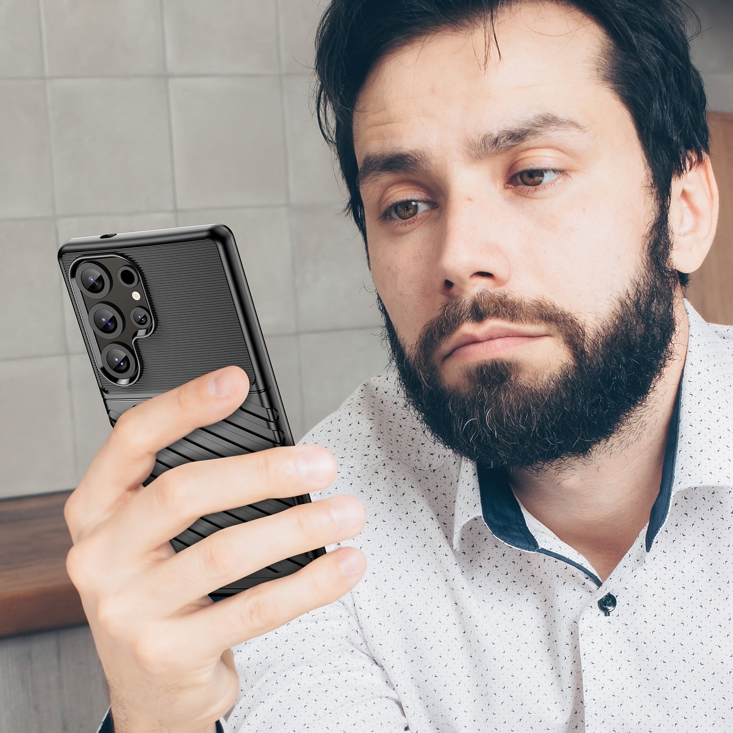 Un hombre sosteniendo un teléfono, mirando la pantalla con una expresión preocupada, en interiores.