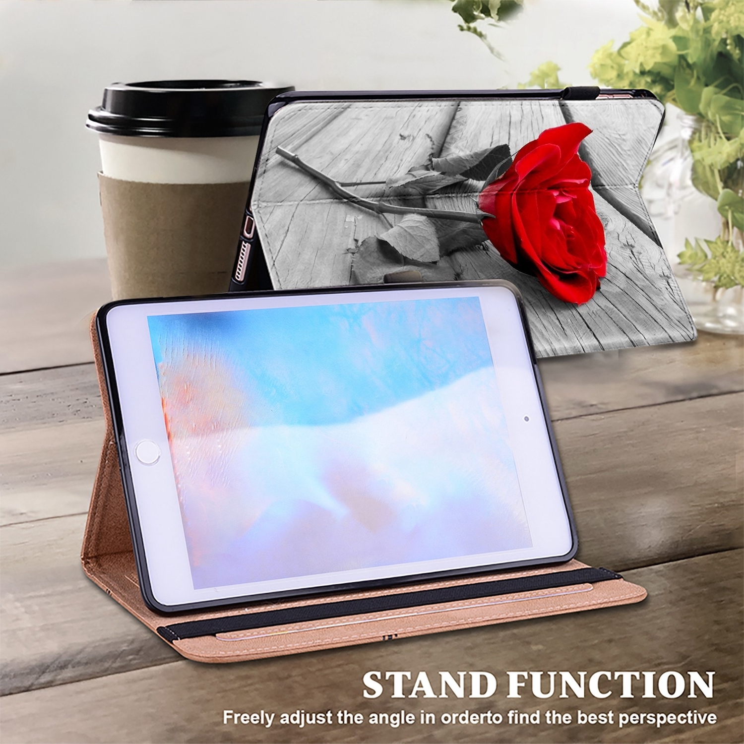 Tablet in Hülle, rote Rose und Kaffeetasse auf dem Tisch, ein Schwarz-Weiß-Bild einer Rose an der Wand.