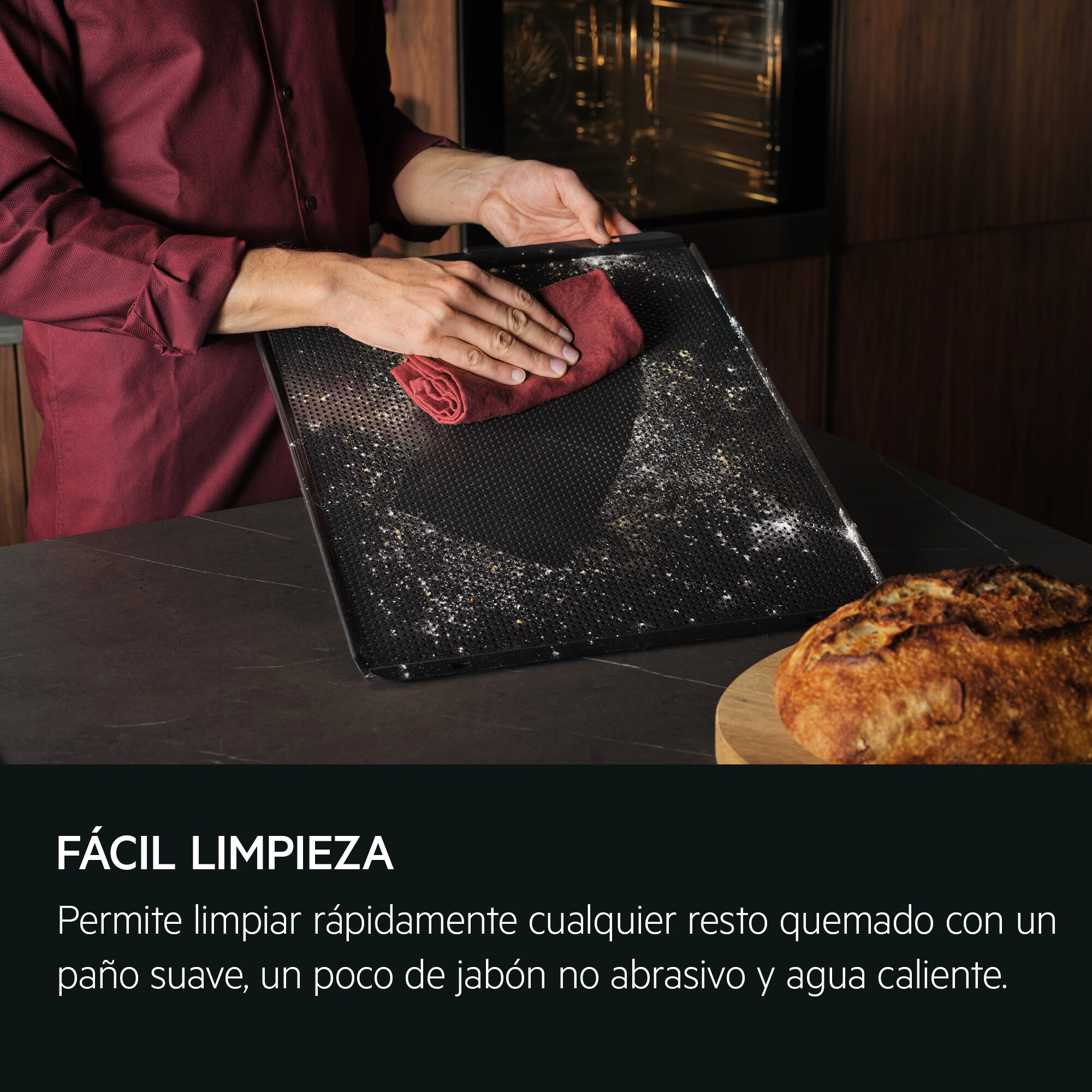 Persona limpiando bandeja de horno sucia con paño rojo. Pan a la derecha.