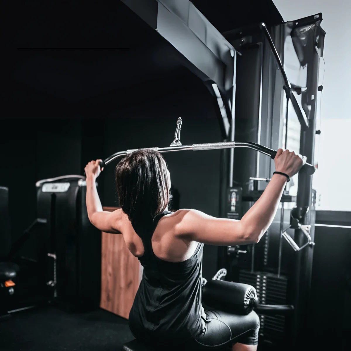 Une femme faisant des tractions dorsales dans une salle de sport, utilisant une barre argentée.