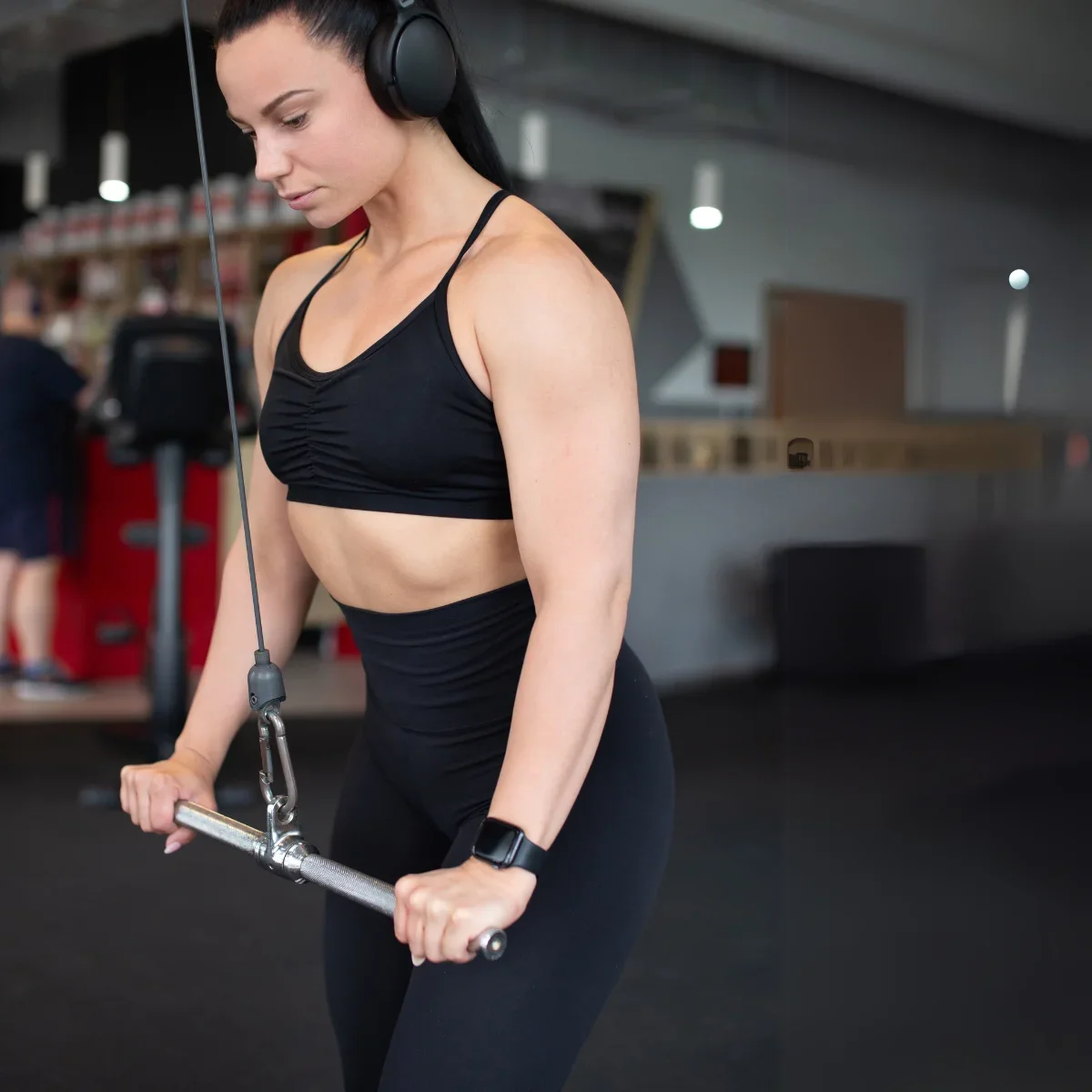A woman in a gym doing triceps extensions using a silver bar.