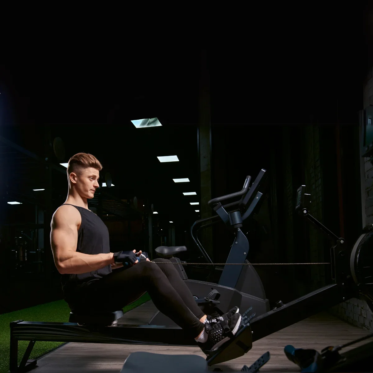 A man is rowing on a machine in a gym, side view.